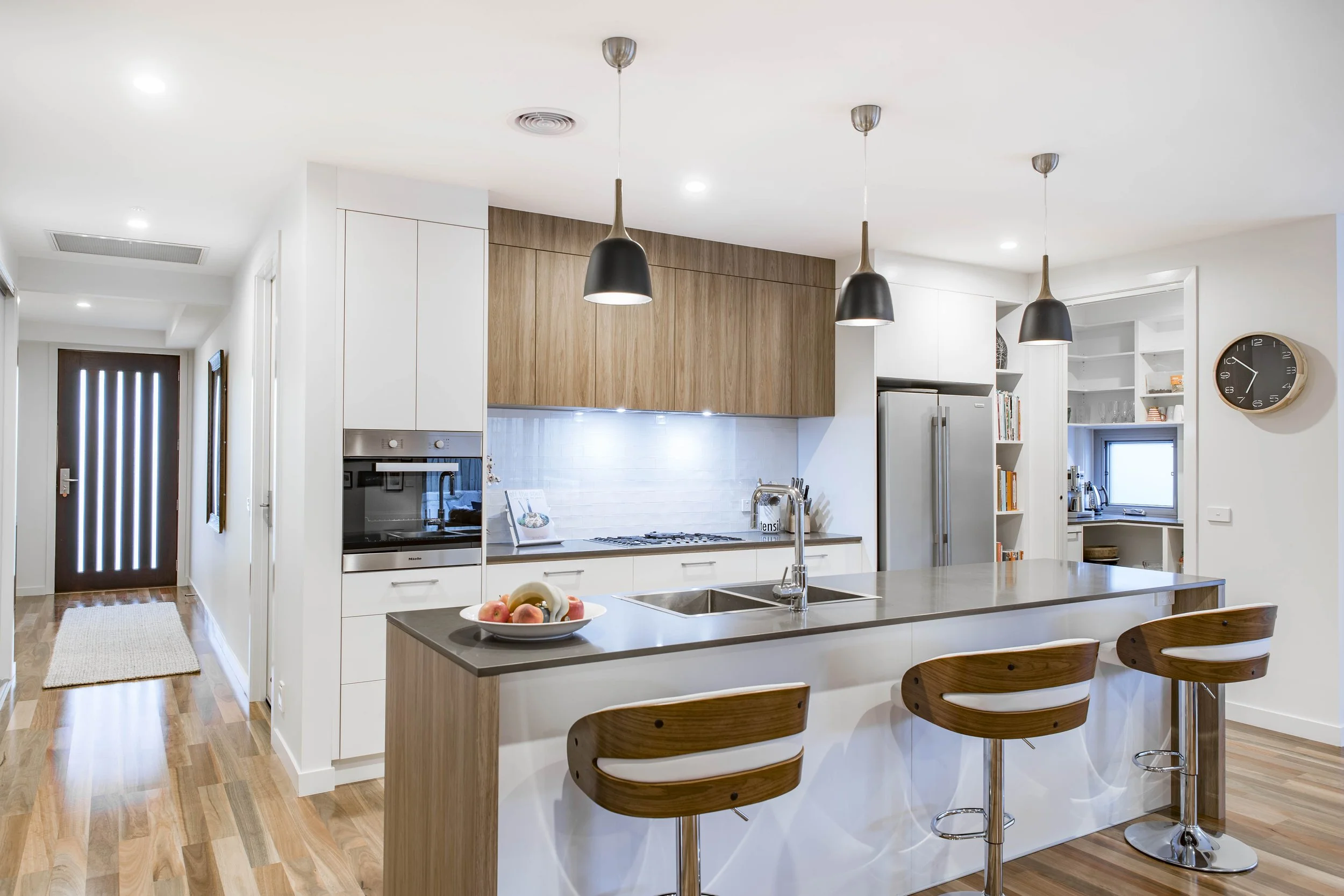 Modern kitchen with white cabinets, wooden accents, a kitchen island with fruit bowl, and black pendant lights.