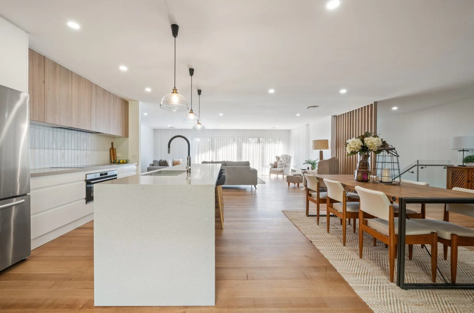Open-concept kitchen and living room with wooden floors, white walls, modern fixtures, dining table with chairs, and a cozy seating area with sofas and armchairs.