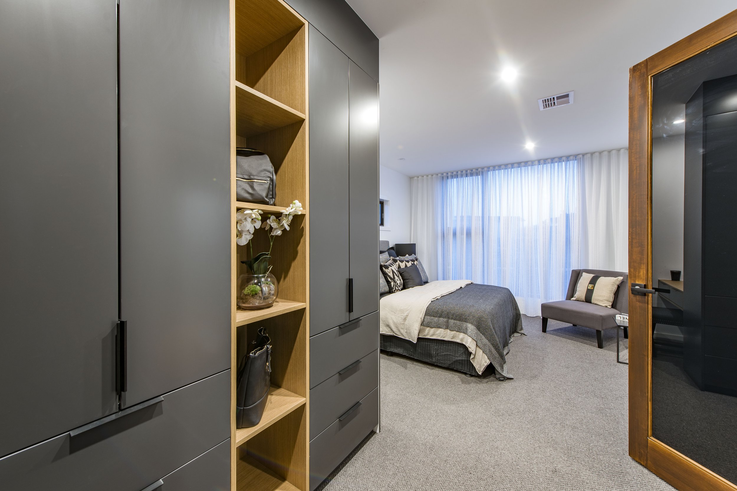 Modern bedroom with gray furniture, a bed, armchair, and large window with white curtains.