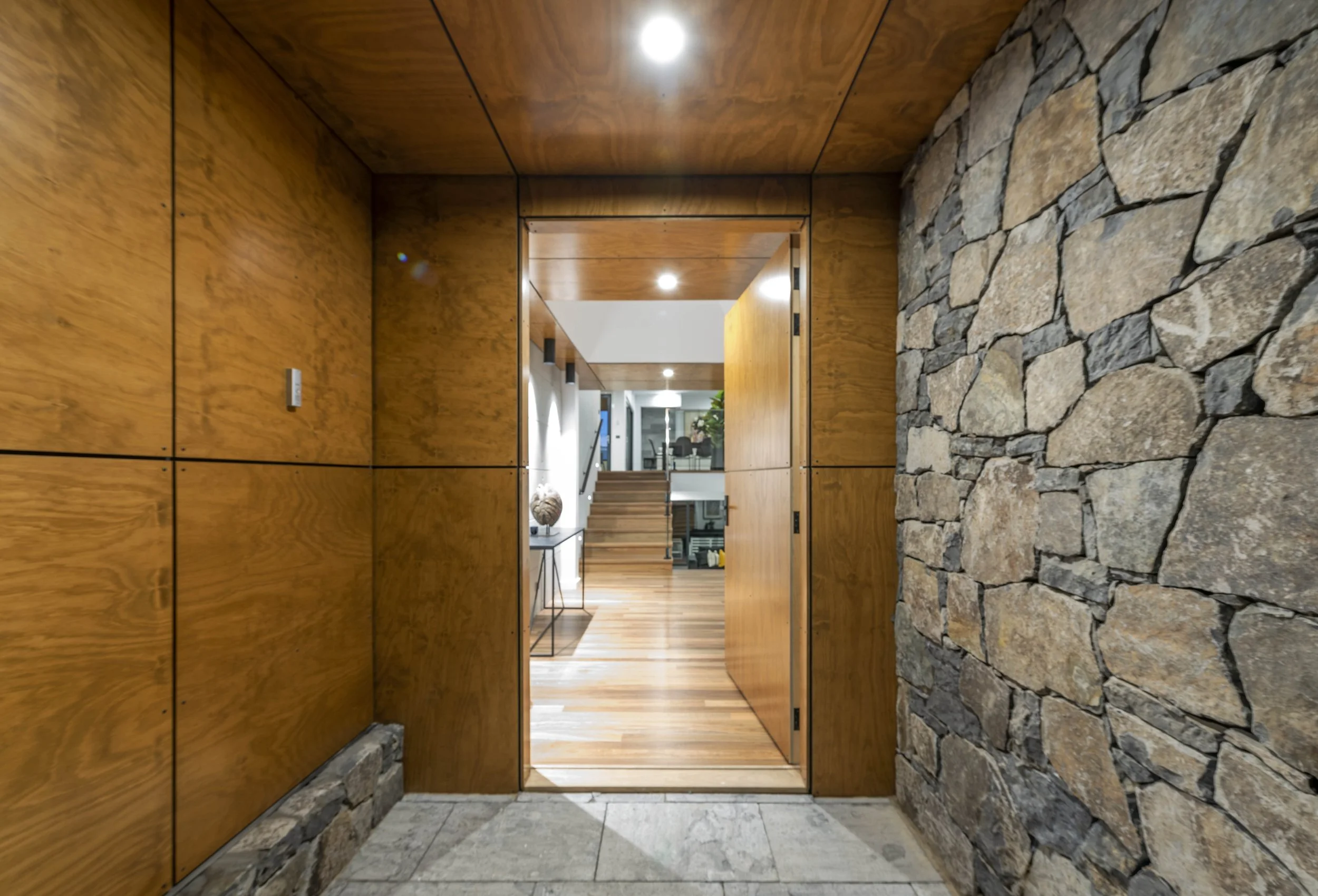Interior view through a wooden doorway with stone walls on the sides, leading into a modern room with wood flooring and contemporary furniture.