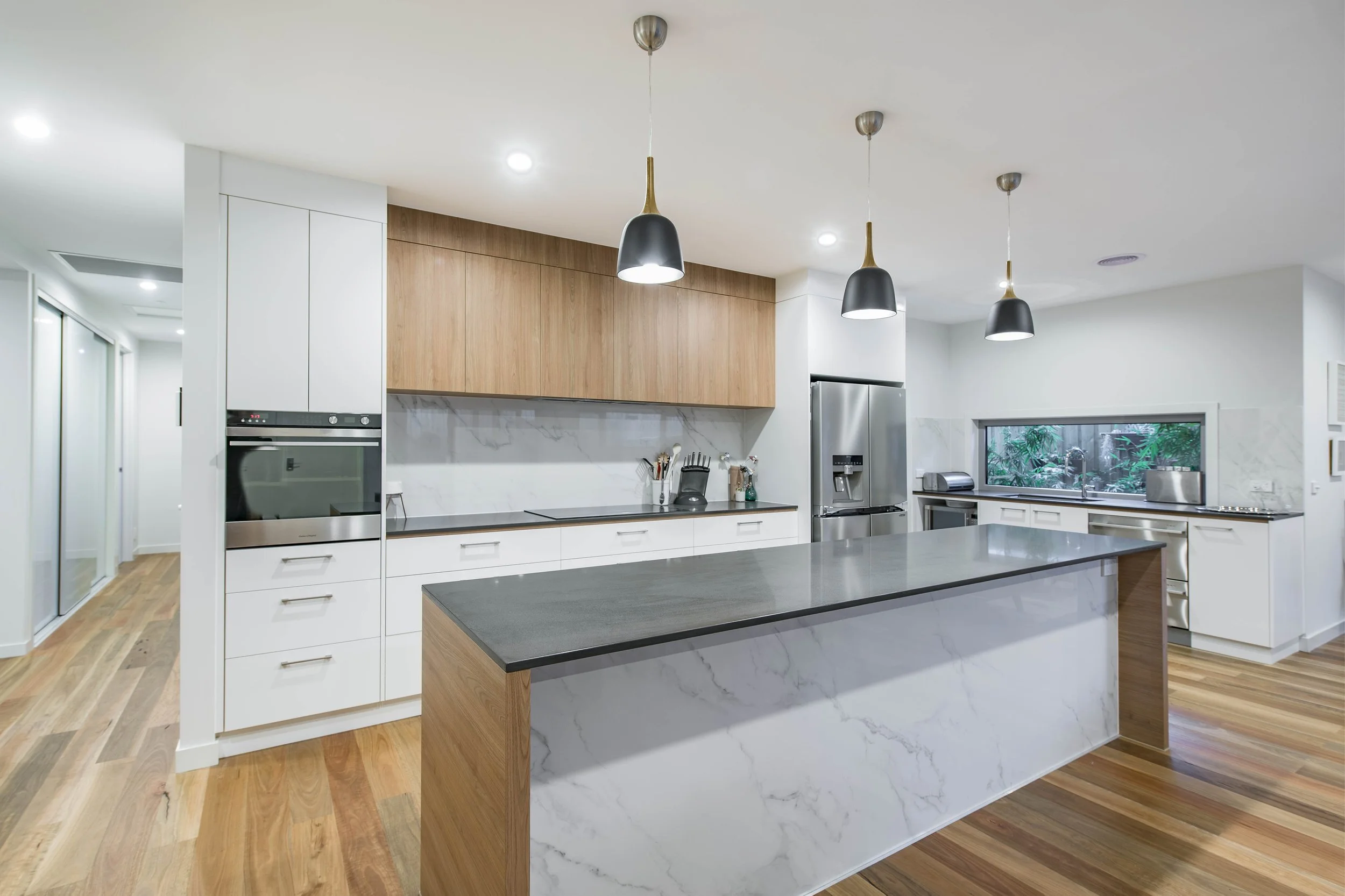 Modern kitchen with white cabinetry, wooden accents, marble island, stainless steel appliances, pendant lighting, and hardwood floors.