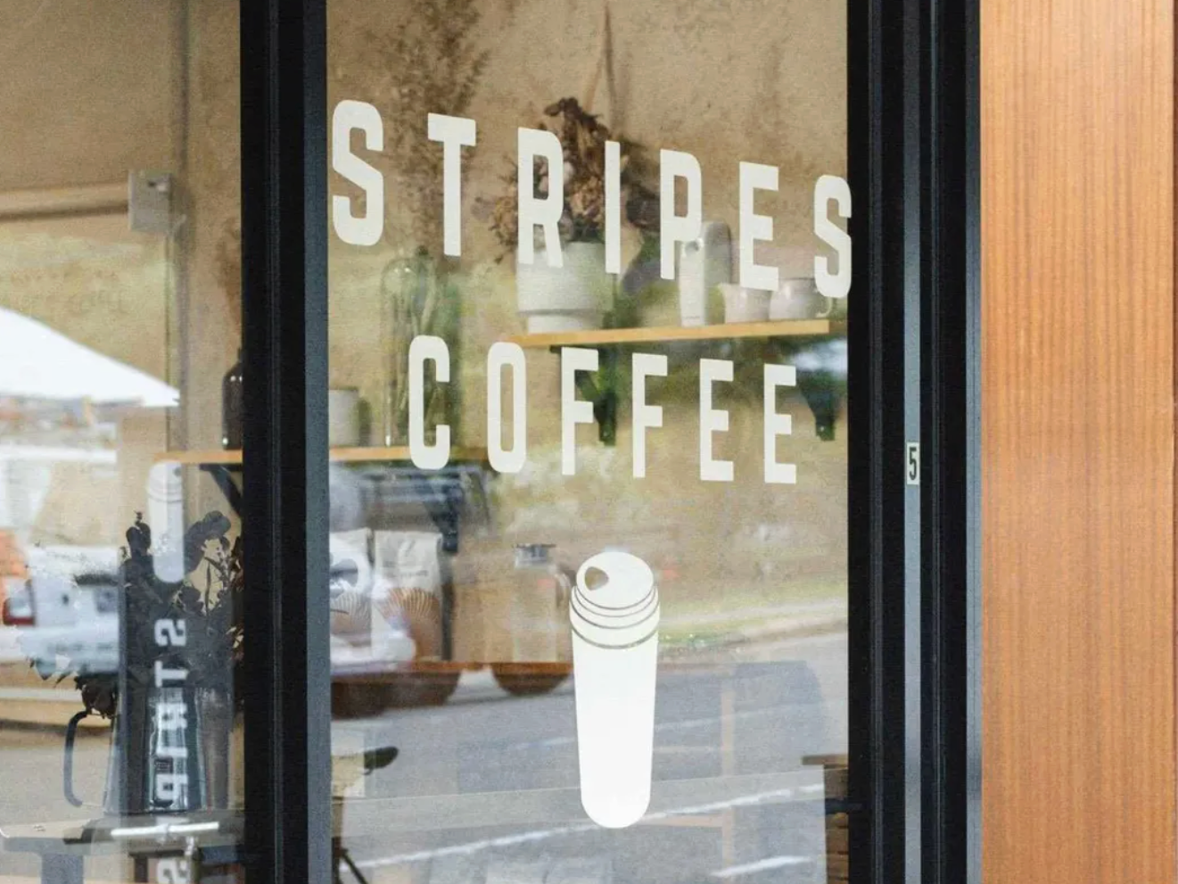 Glass window with white text that reads "Stripes Coffee" and a minimalist illustration of a coffee cup, with a reflection of the street outside.