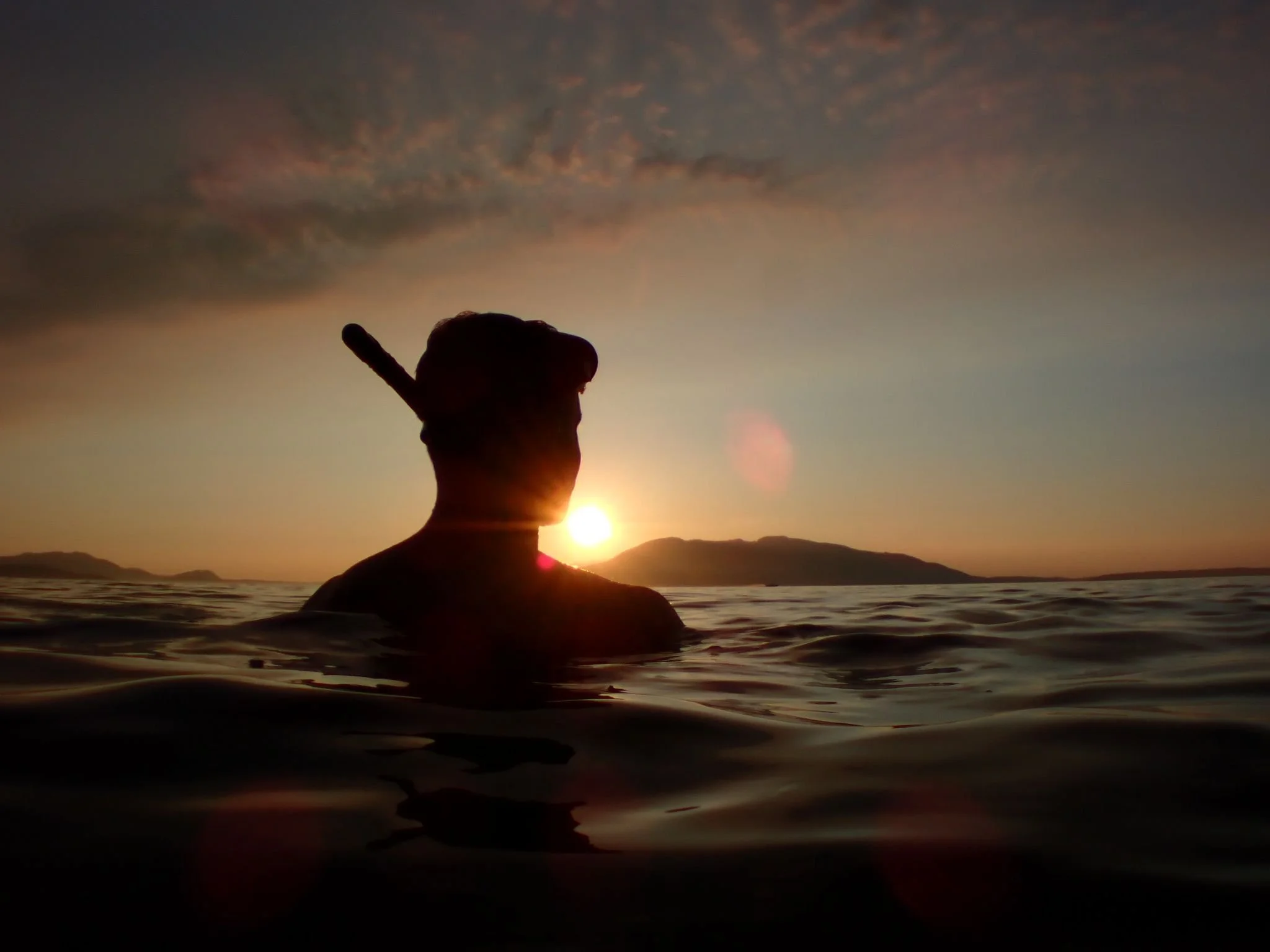 Silhouette of a freediver partially submerged in water during sunset, with a Lummi island in the background.