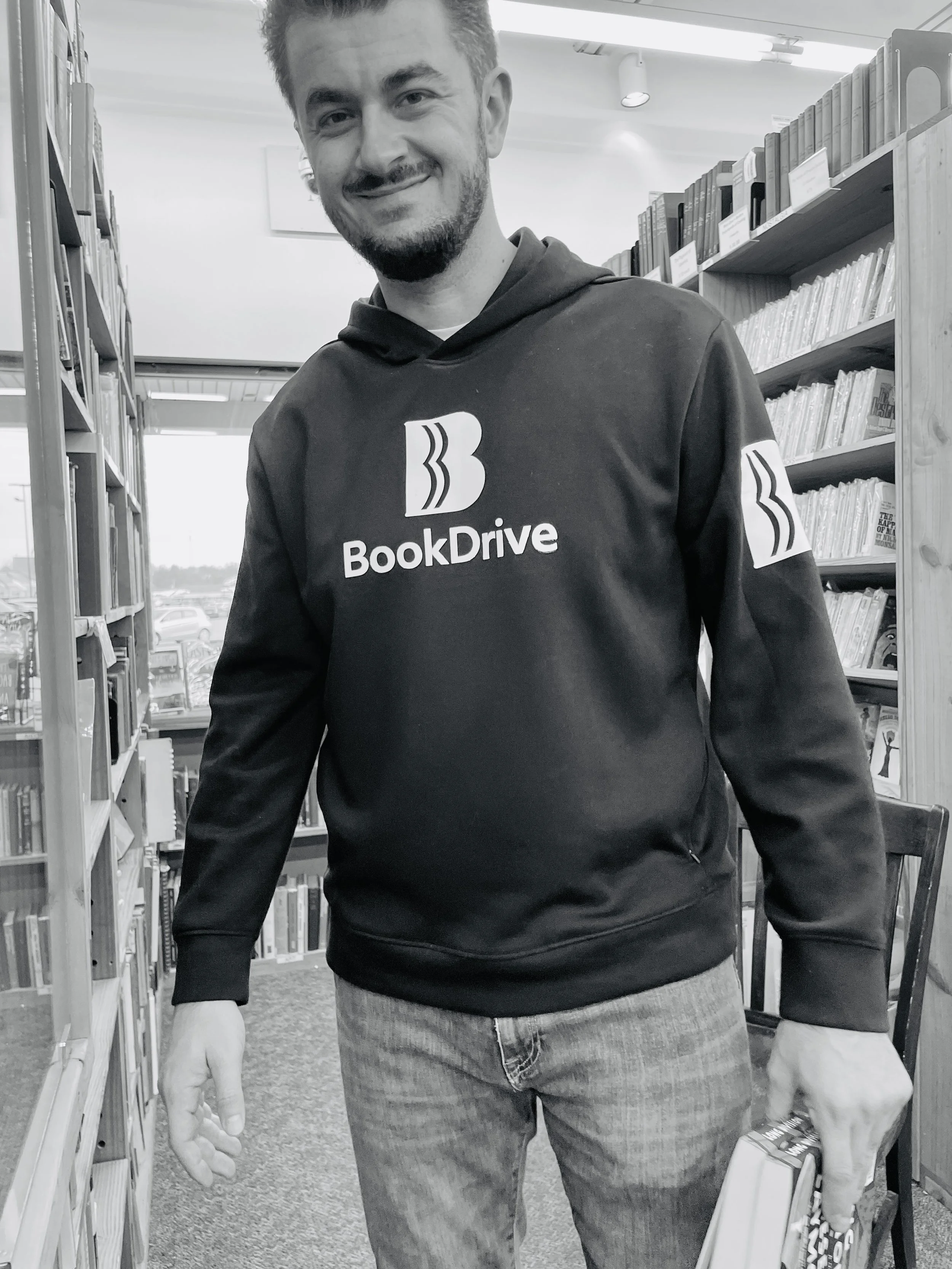 Founder of BookDrive wearing a BookDrive hoodie while standing between bookstore shelves and holding books