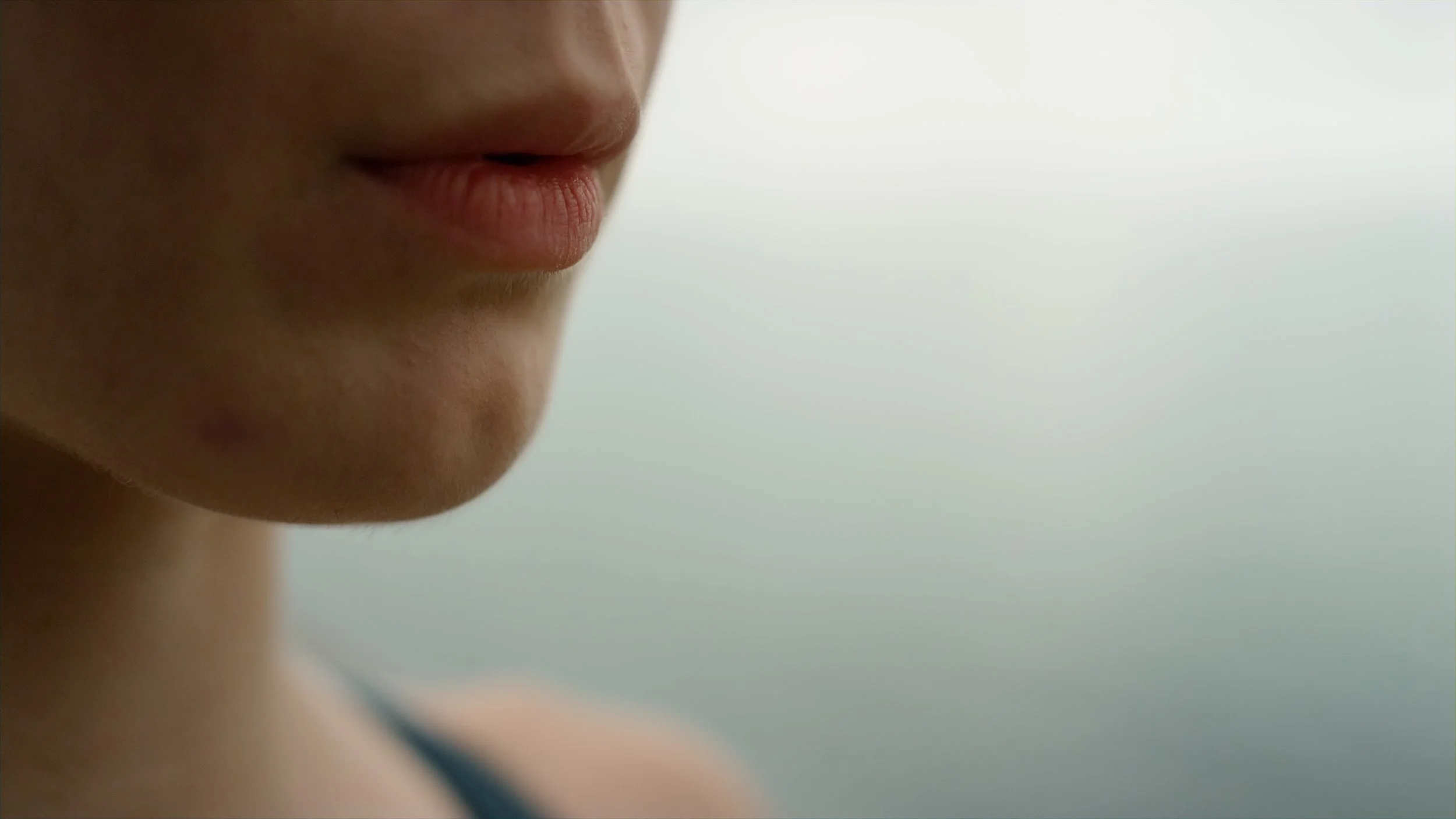 Close-up of a person's lips and chin against a plain, light background.
