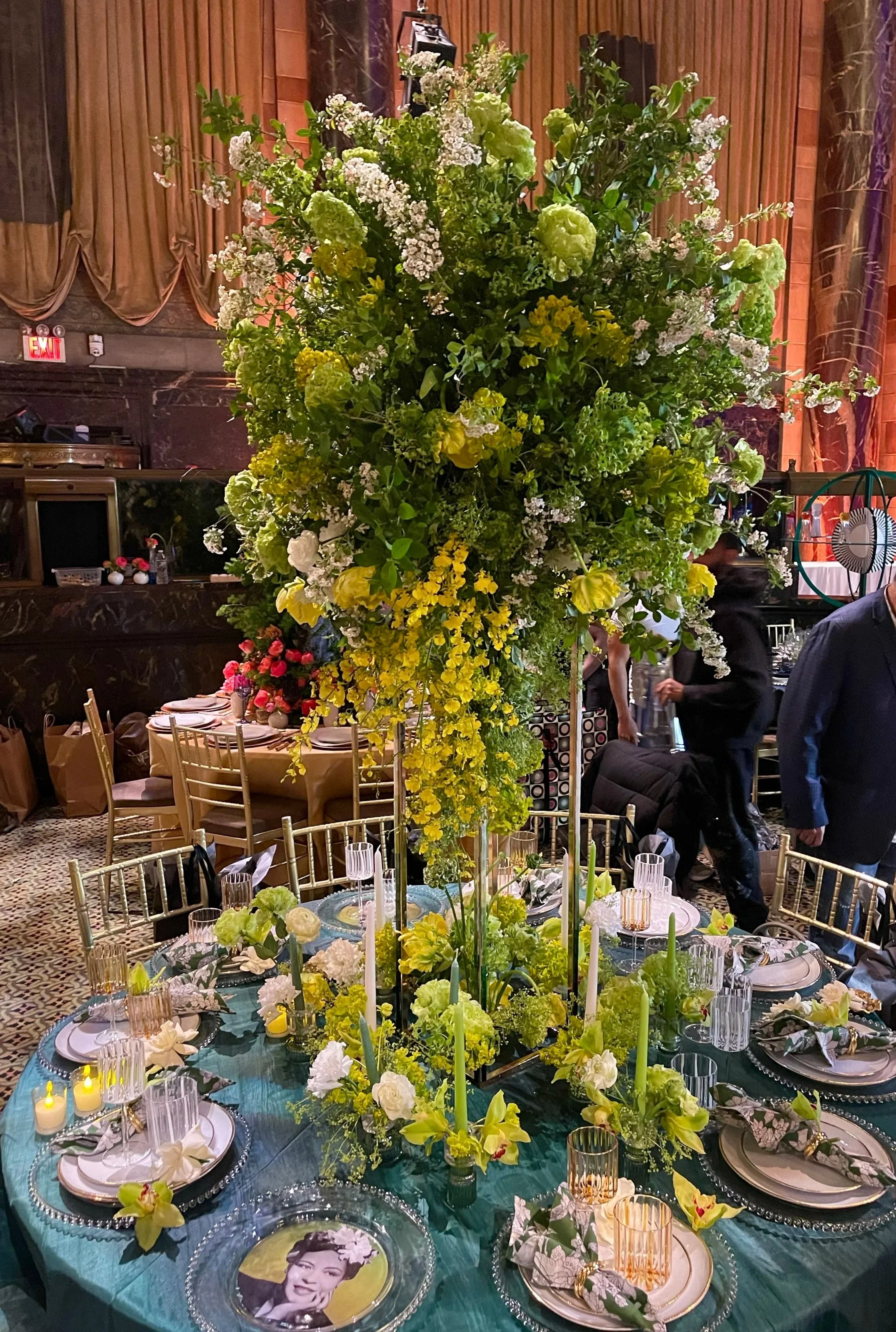 A tall floral centerpiece with green, white, and yellow flowers decorated on a banquet table at an event or wedding reception.