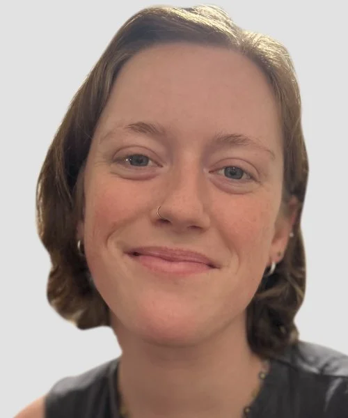 Close-up of a smiling woman with short brown hair, blue eyes, wearing silver hoop earrings and a nose ring.