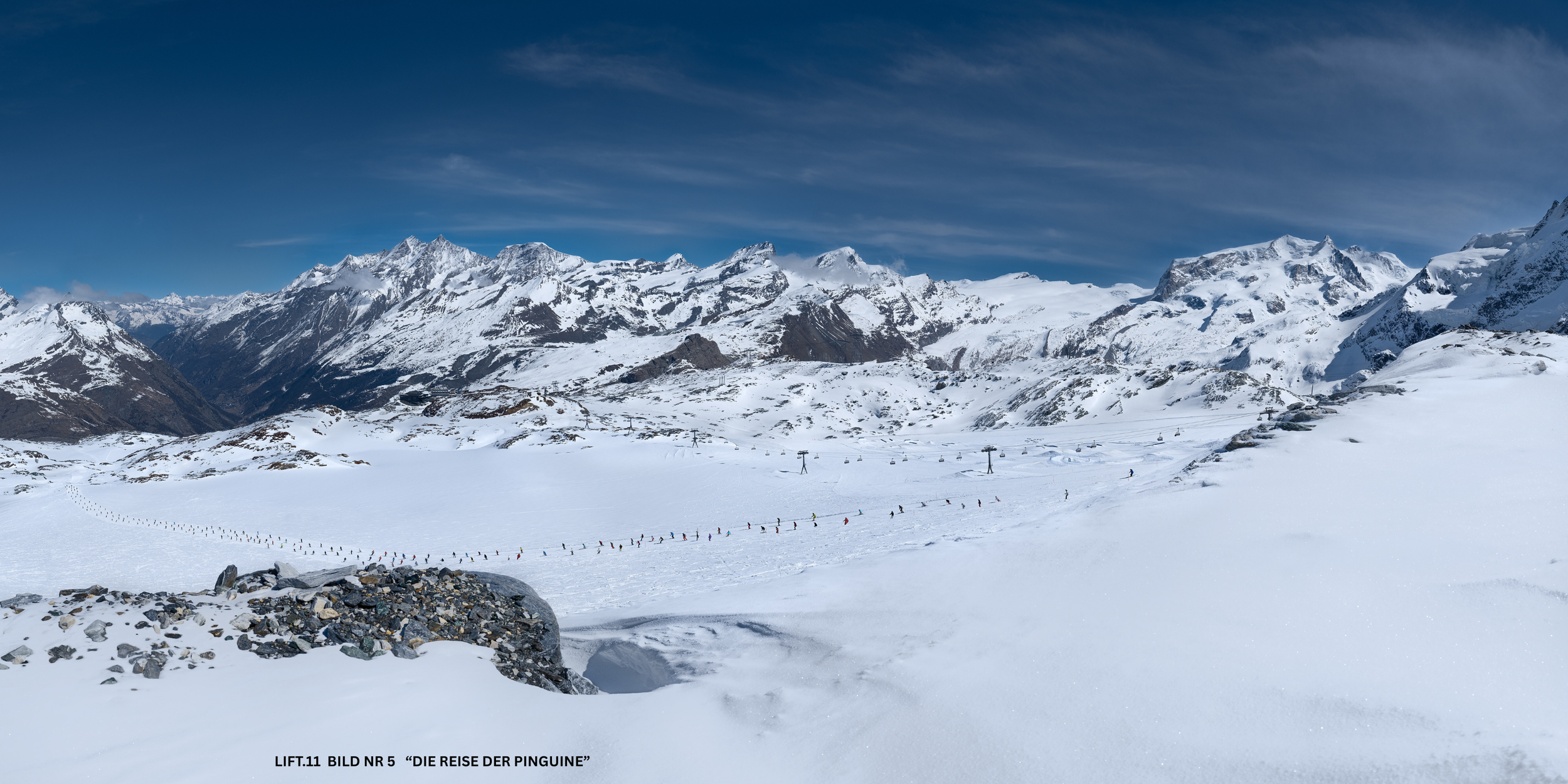 Schneebedeckte Berge mit Skiliften und Skifahrern in der Winterlandschaft, blauer Himmel.