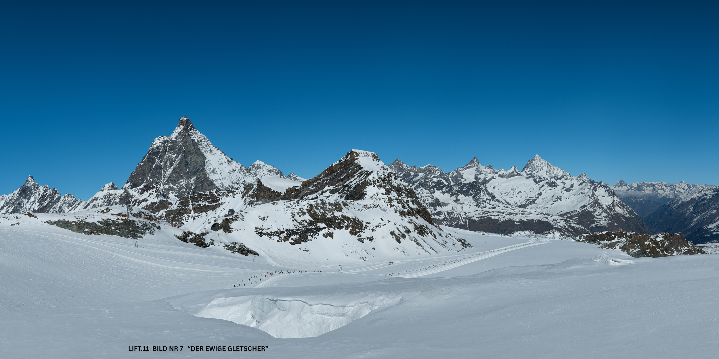 Schneebedeckte Berge unter klarem blauen Himmel im Skigebiet, mit Spuren im Schnee im Vordergrund.