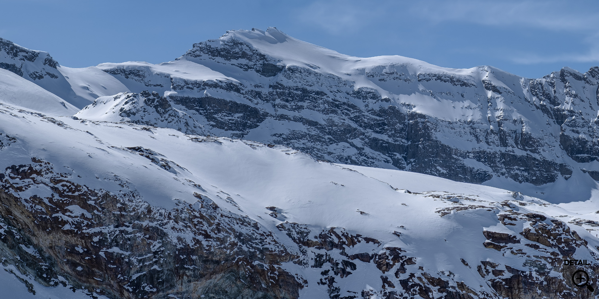 Schneebedeckte Berge mit Felsen unter blauem Himmel.