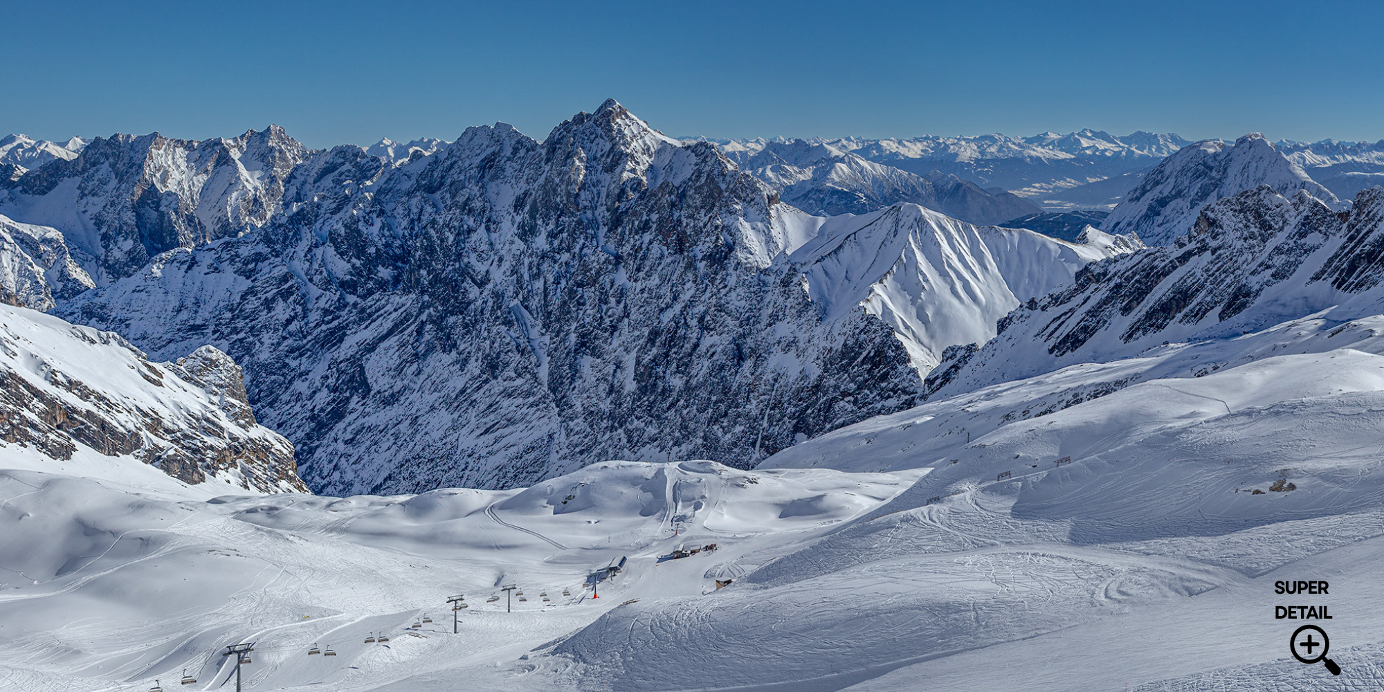 Schneebedeckte Berge in den Alpen bei klarem Himmel, Skilift mit Sesseln im Vordergrund, winterliche Skiregion in Österreich oder Schweiz.