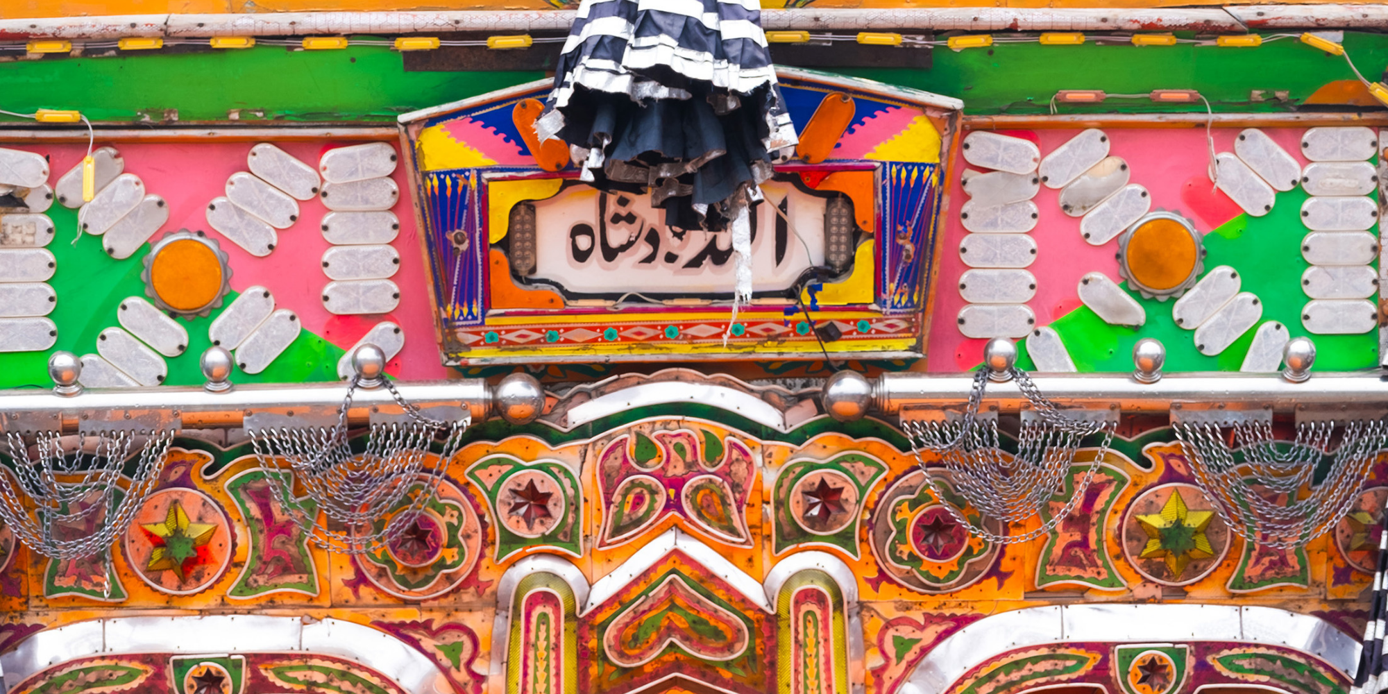 Bunt bemalte Achterbahn mit Lichtern, metallischen Dekorationen und einem Tuch, das an der Spitze hängt, in einem Freizeitpark.