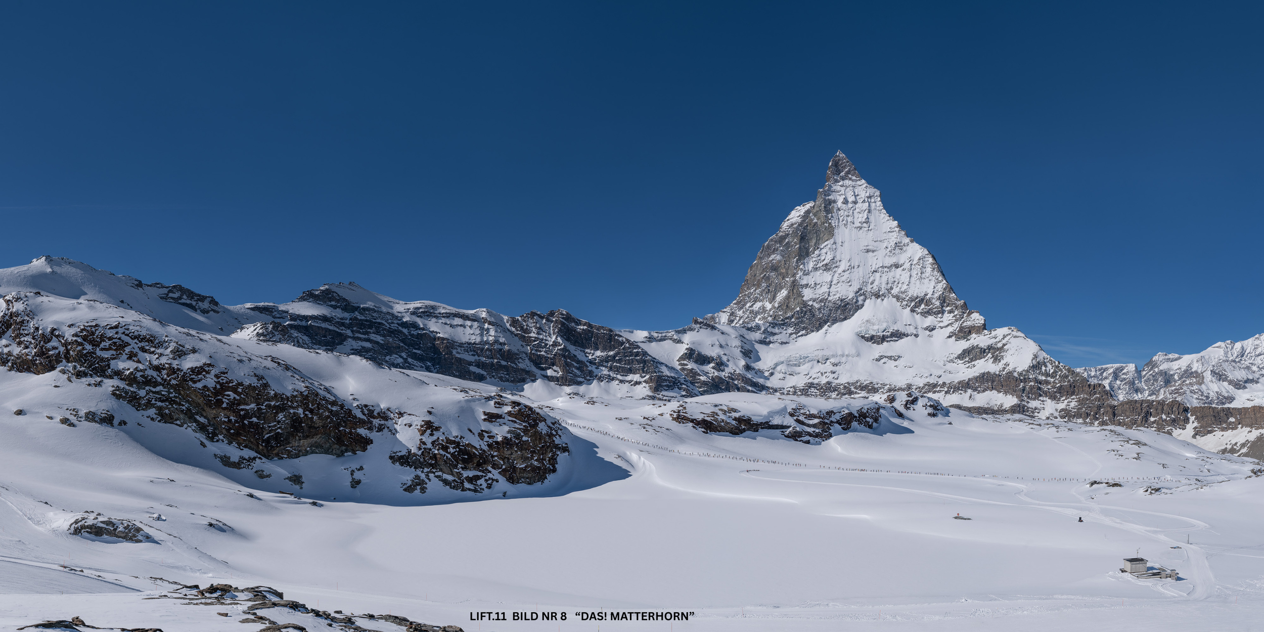 Blick auf die Skipiste und das Matterhorn im verschneiten Hochgebirge bei klarem blauen Himmel.