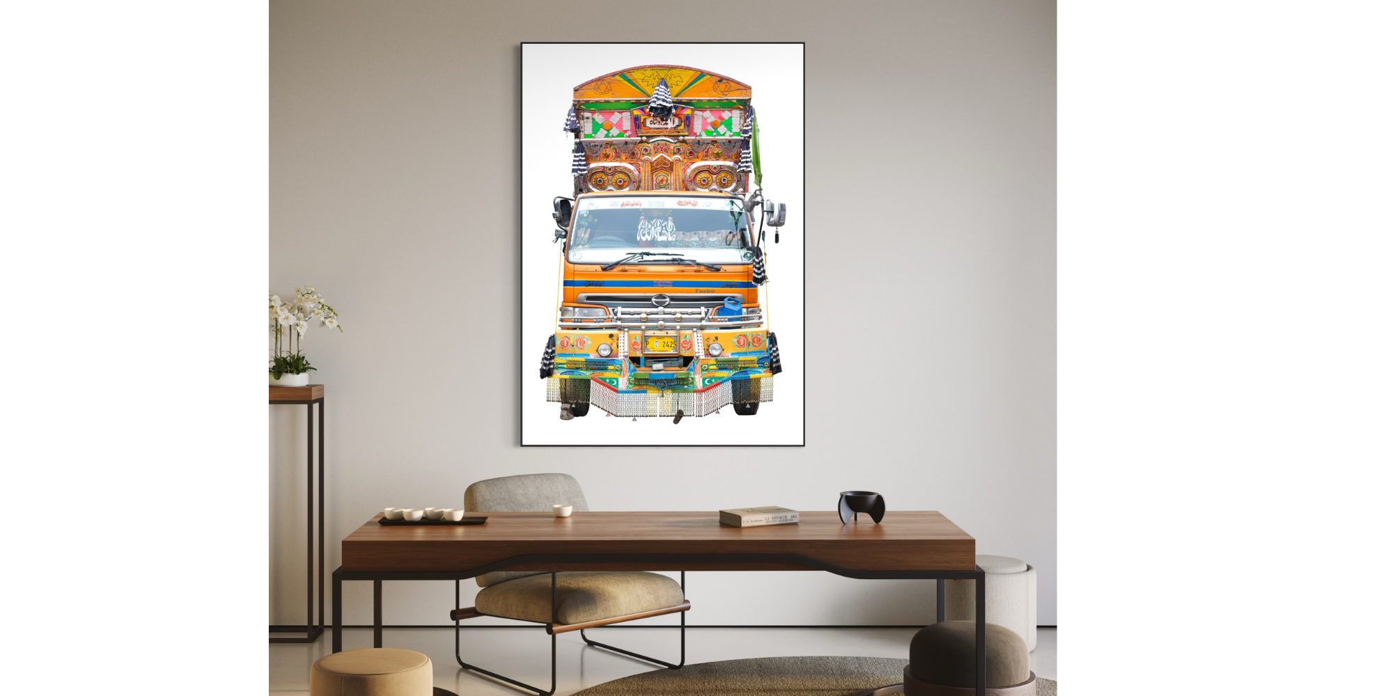 Ein farbenfrohes Kunstwerk eines dekorierten Lastwagens hängt an einer weißen Wand in einem Wohnzimmer, mit einem Holzschreibtisch, einem Stuhl und Dekorationsgegenständen.