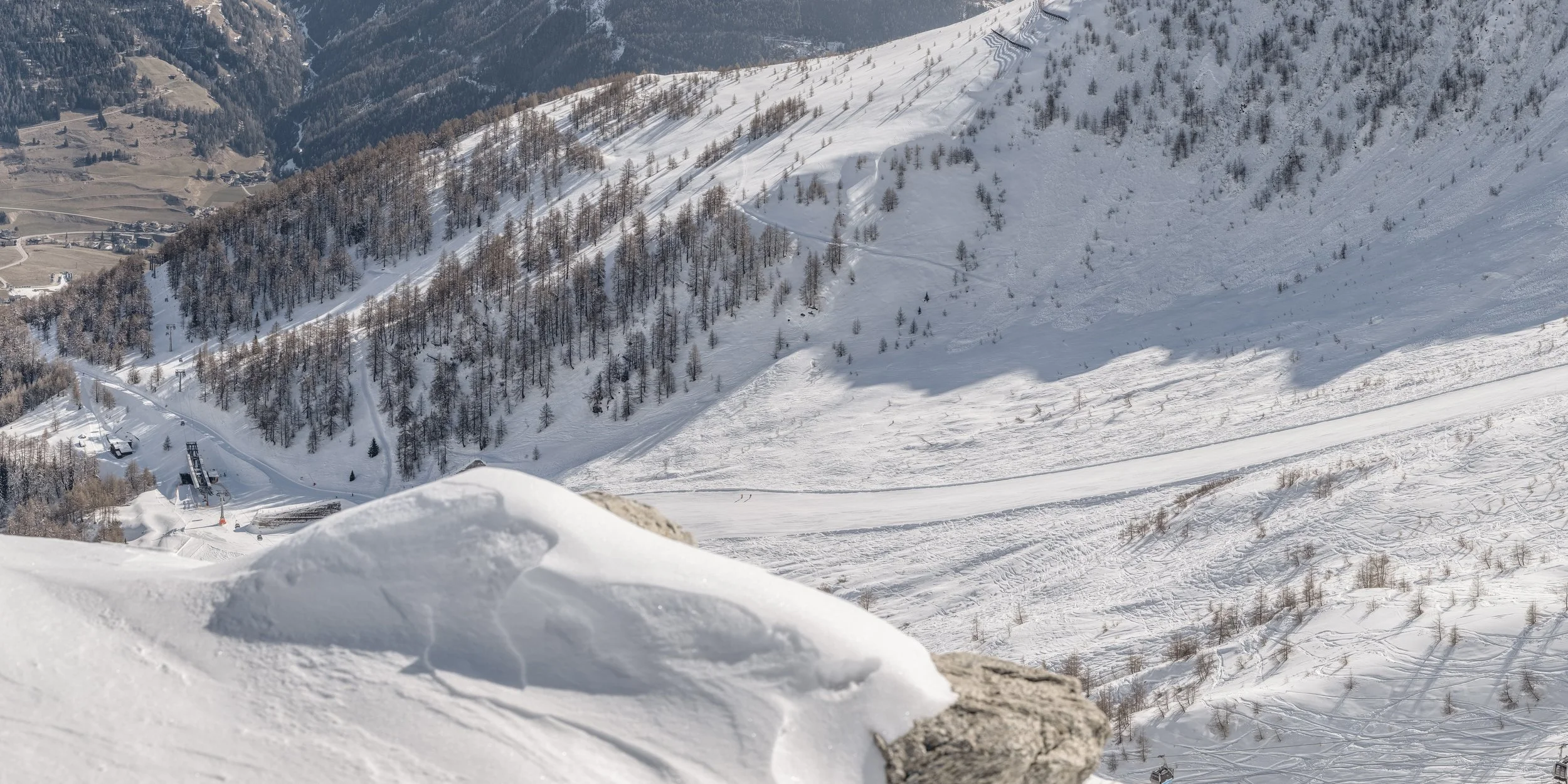Schneebedeckte Berge und Hänge in den Alpen mit Skifahrern und Skiliften im Tal, Blick von einer höheren Position aus.
