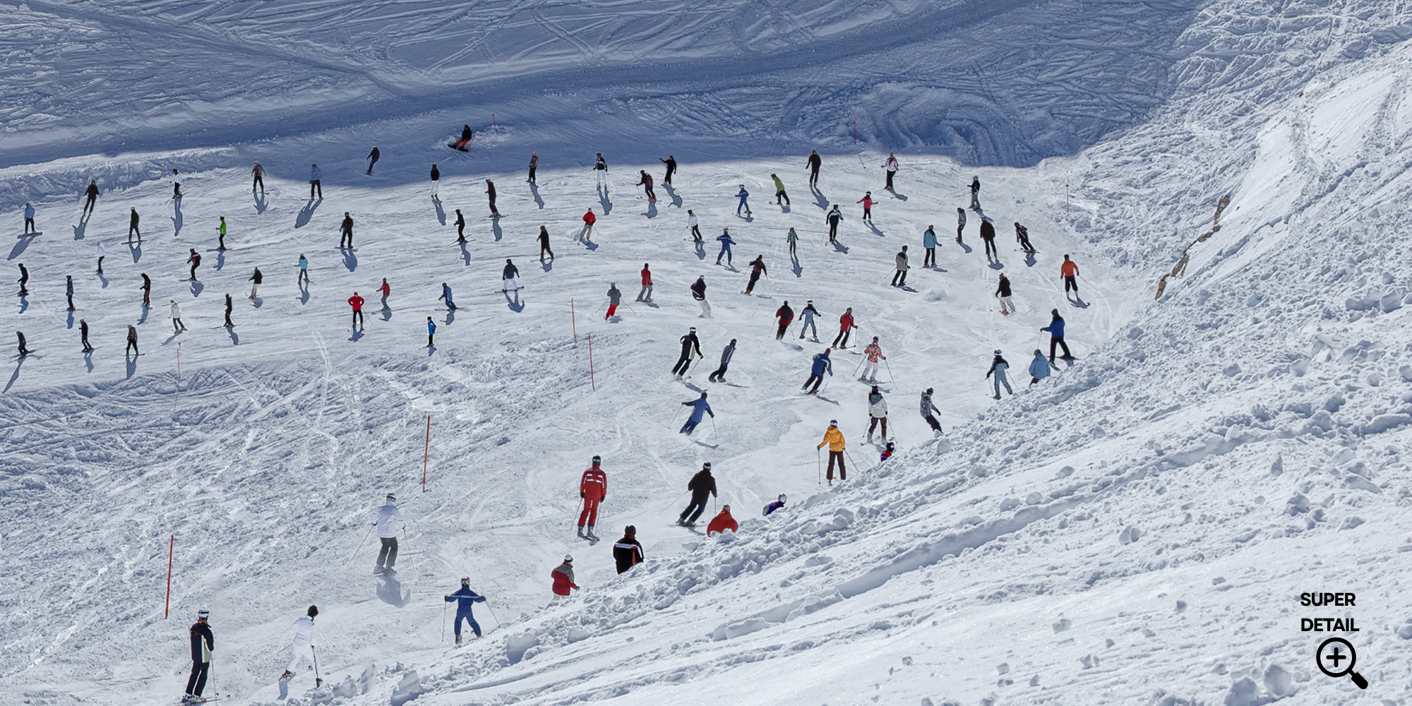 Viele Skifahrer auf einer verschneiten Skibergfeld, die Abfahrt machen, im Hintergrund eine Schneefläche mit Spuren und Abfahrtspisten.