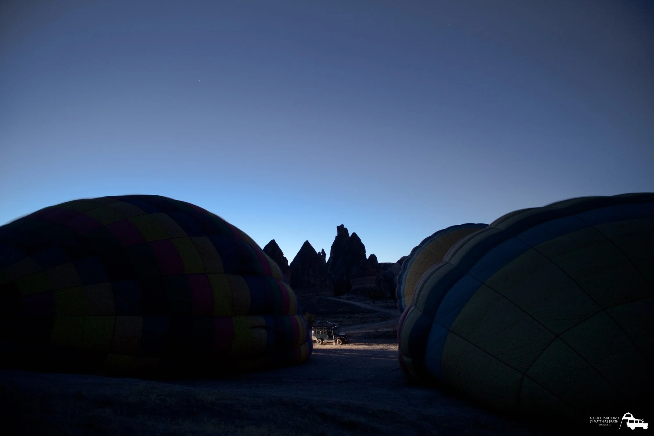 Absichtliches Foto von Heißluftballons im Morgengrauen, mit dunklen Silhouetten der Ballons und einer Gebirgskette im Hintergrund