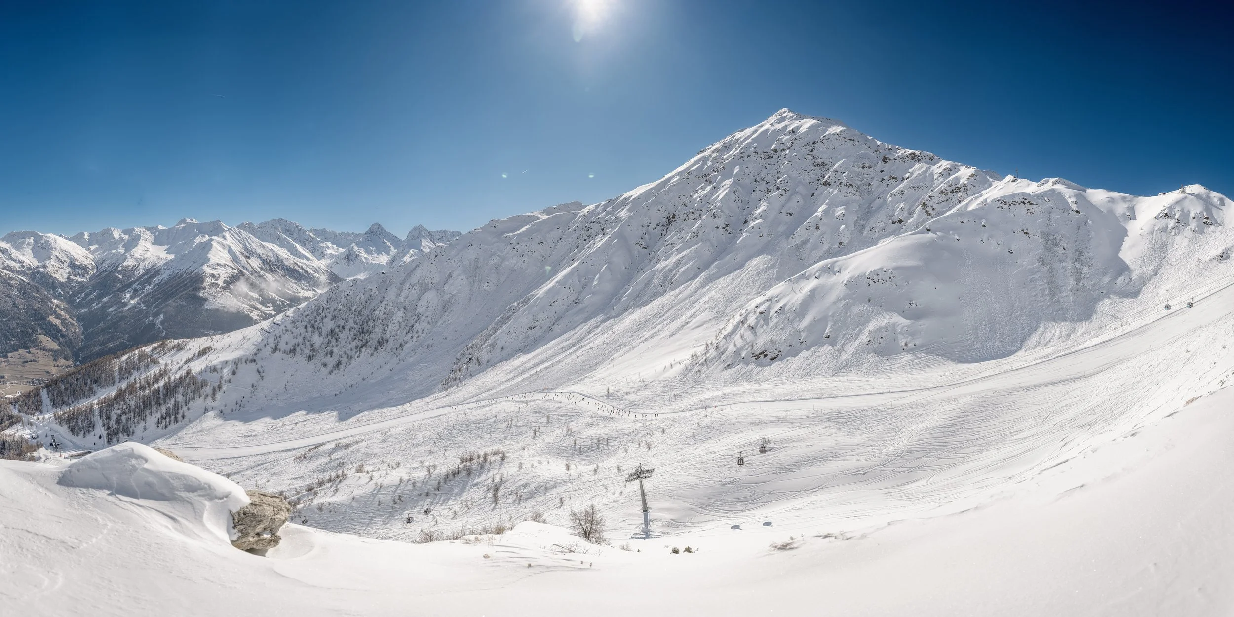 Schneebedeckte Berge und Skipisten in den Alpen, sonniger tag, Skilift im Vordergrund.