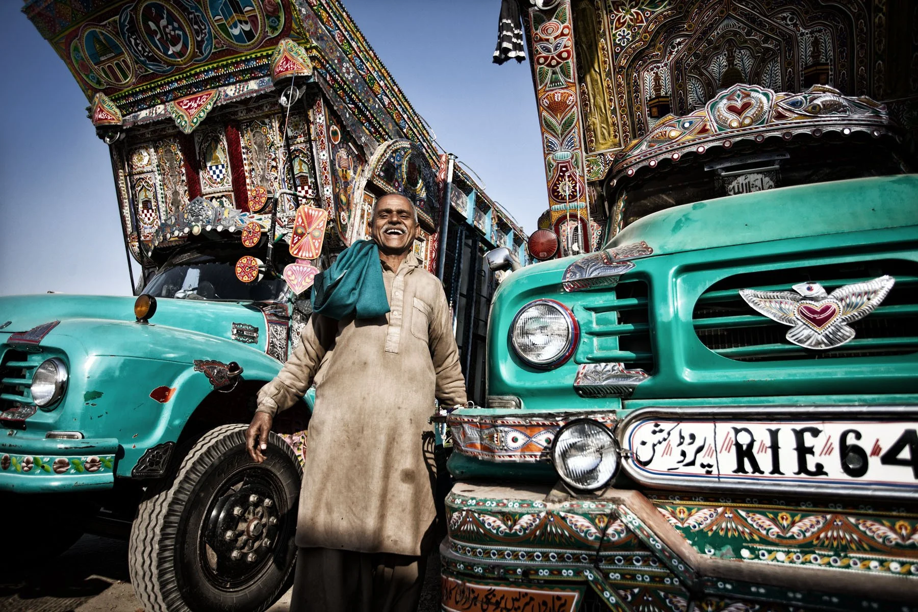 Ein lachender Mann steht vor bunten, reich verzierten Lastwagen in Pakistan.