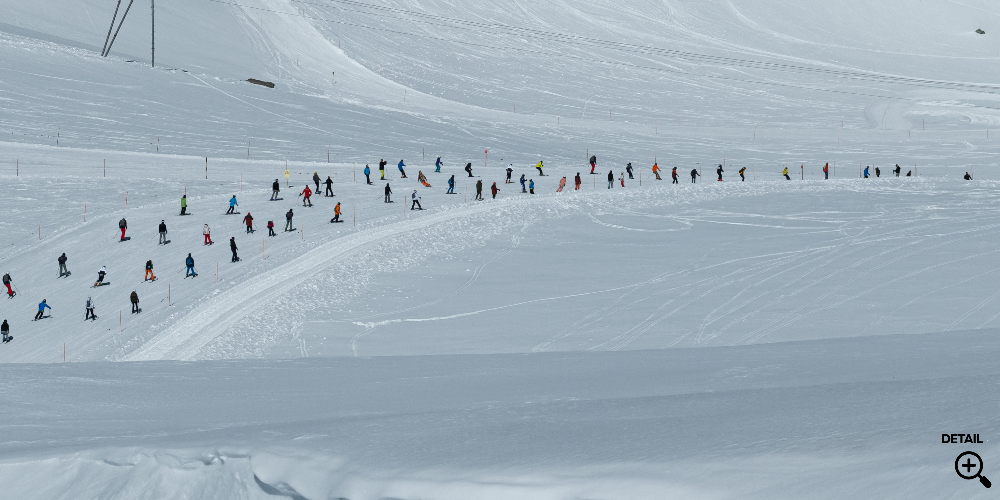 Viele Skifahrer und Snowboardfahrer auf einer verschneiten Piste im Skigebiet, mit einer geraden Spur in der Mitte, im Hintergrund Skilifte und eine schneebedeckte Berglandschaft