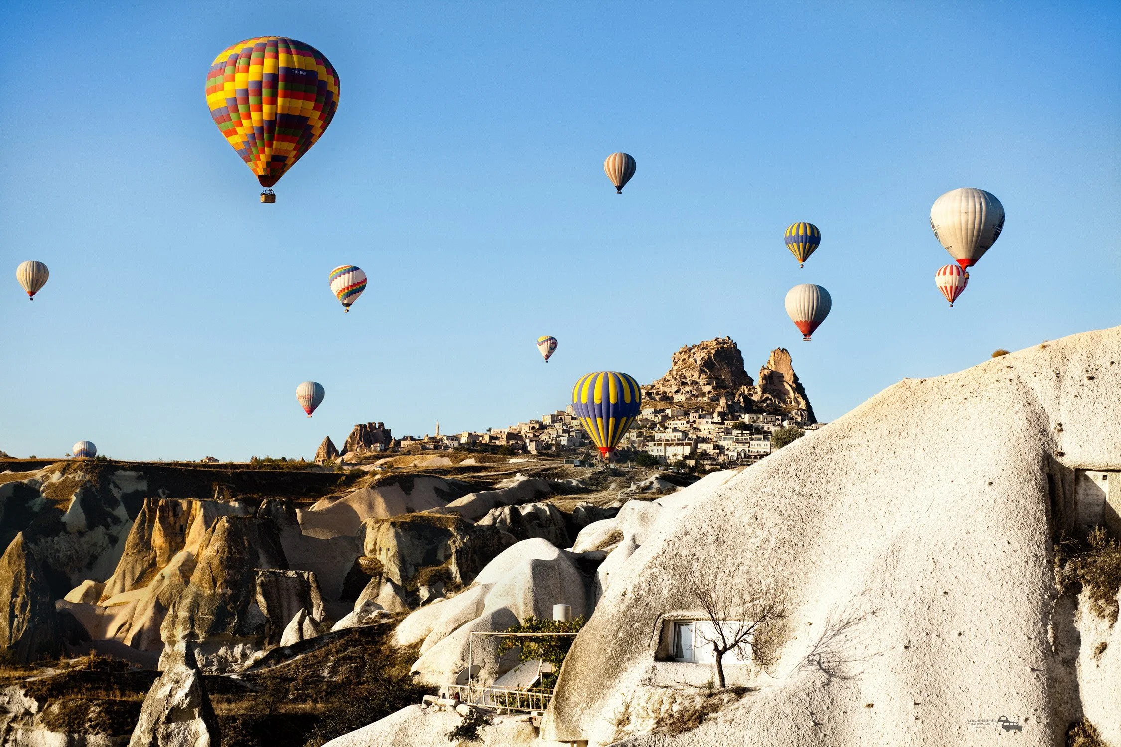 Mehrere bunte Heißluftballons fliegen über einer felsigen Landschaft mit historischen Gebäuden und Felsen.