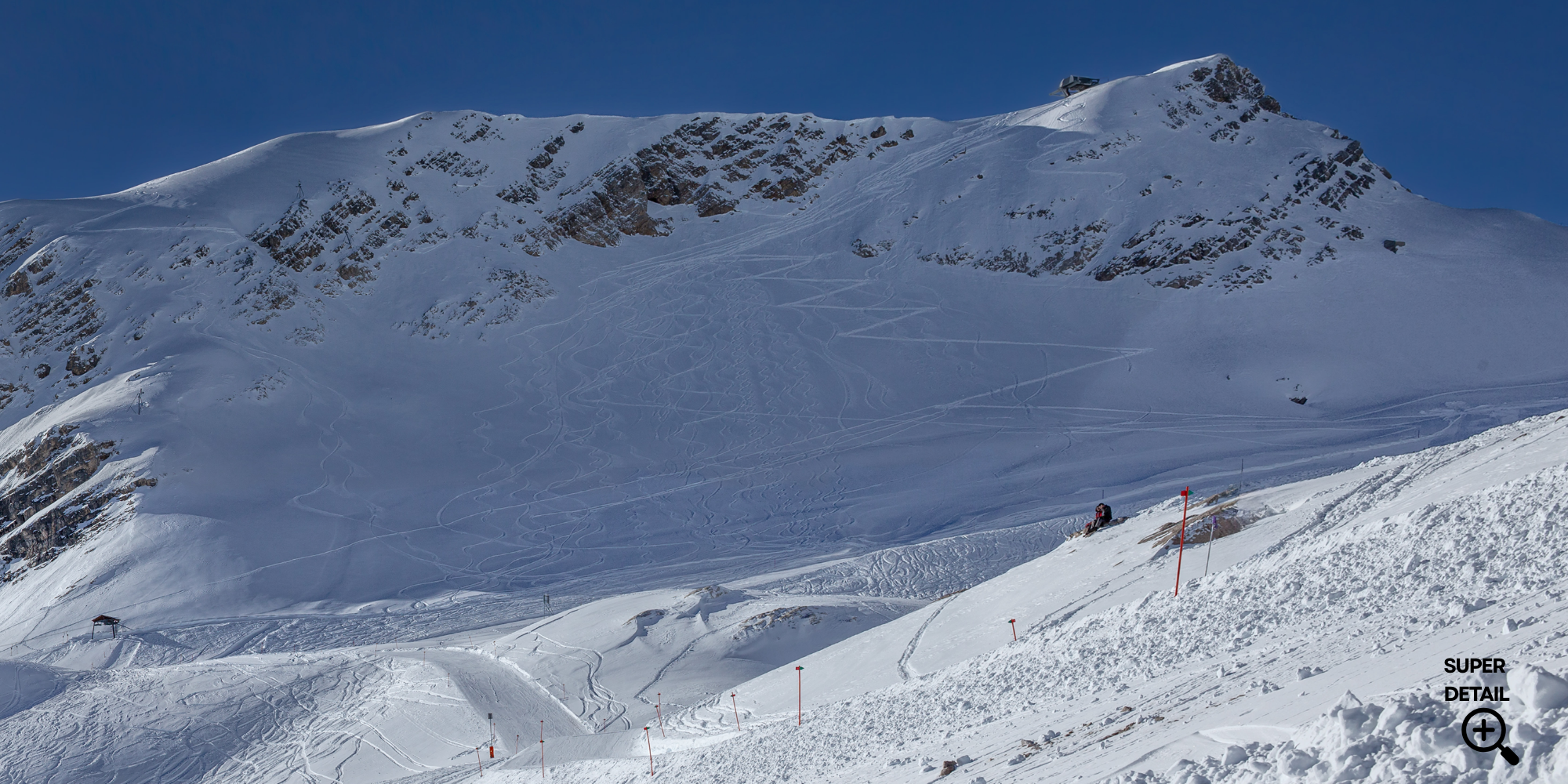 Schneebedeckte Berglandschaft mit Skipisten, Skifahrern und Skilift in einem Wintersportgebiet bei klarem Himmel.