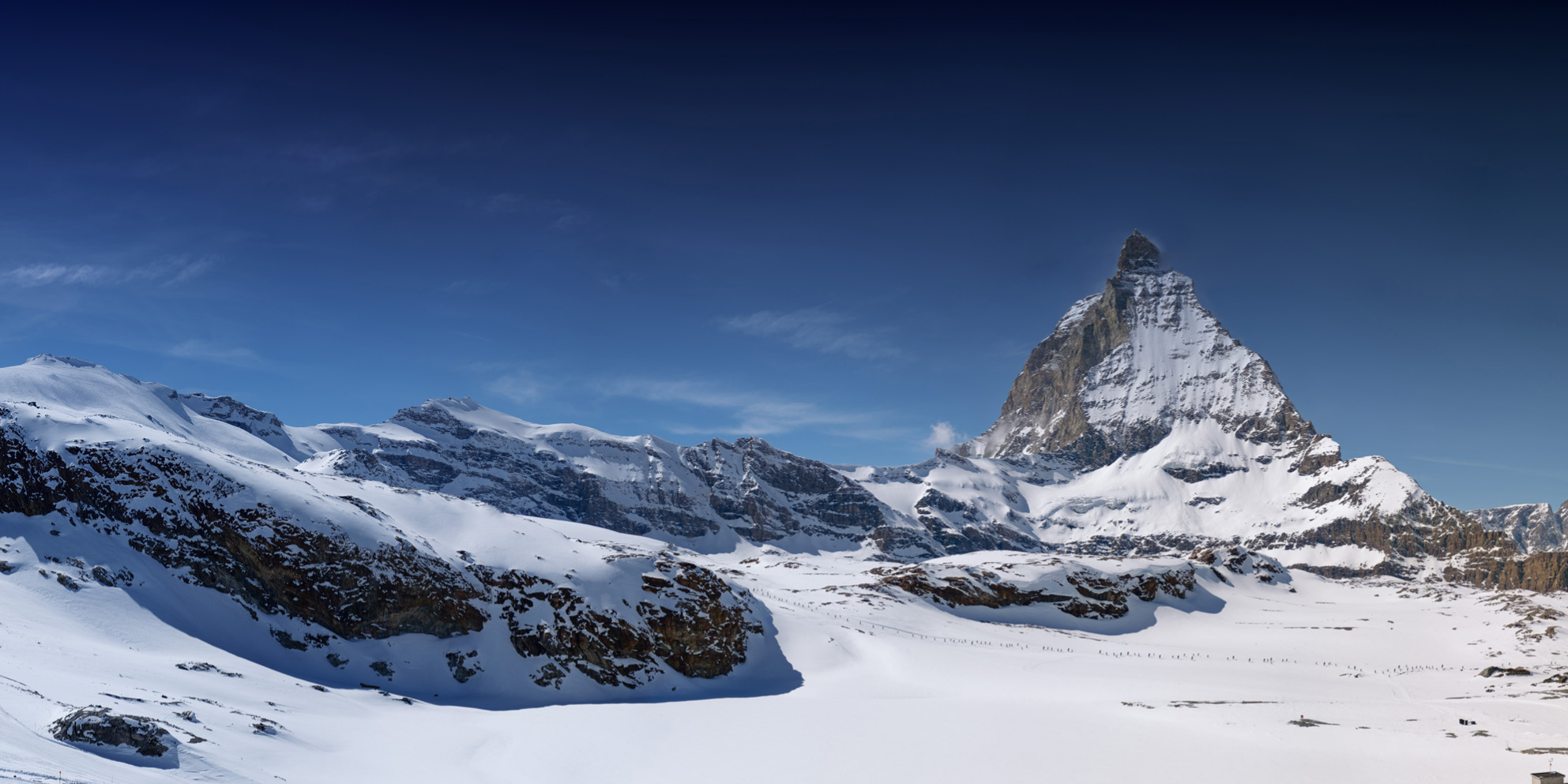 Schneebedeckte Berge unter einem blauen Himmel, charakteristischer Gipfel in der Ferne.