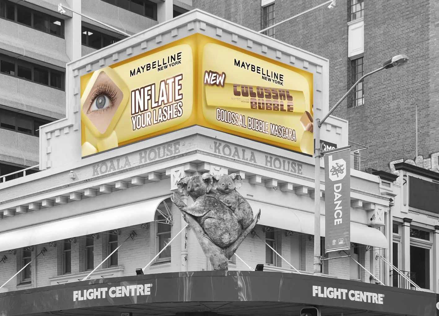 Large digital billboard advertising Maybelline mascara with the slogan "Inflate Your Lashes" and new colossal bubble mascara. The billboard displays an eye with long eyelashes and a yellow background. The building has the name Koala House, and there is a sculpture of a koala on a branch below the billboard. The scene is in an urban setting with nearby buildings, a street lamp, and a banner that says "Dance."
