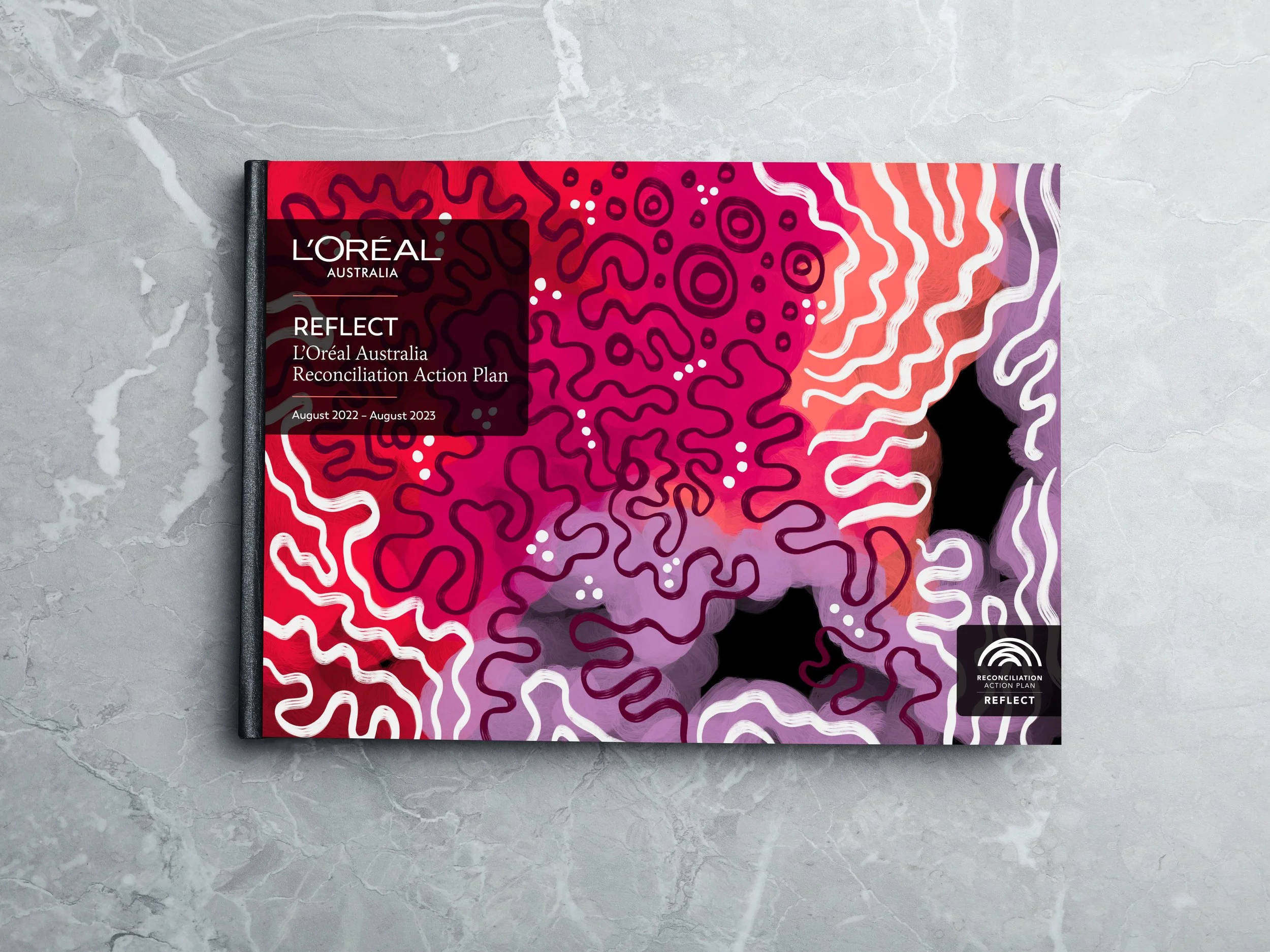 A colorful product packaging featuring abstract line patterns in red, purple, and white, with a black label indicating L'Oréal Australia's Reconciliation Action Plan titled 'Reflect' for August 2022 to August 2023.