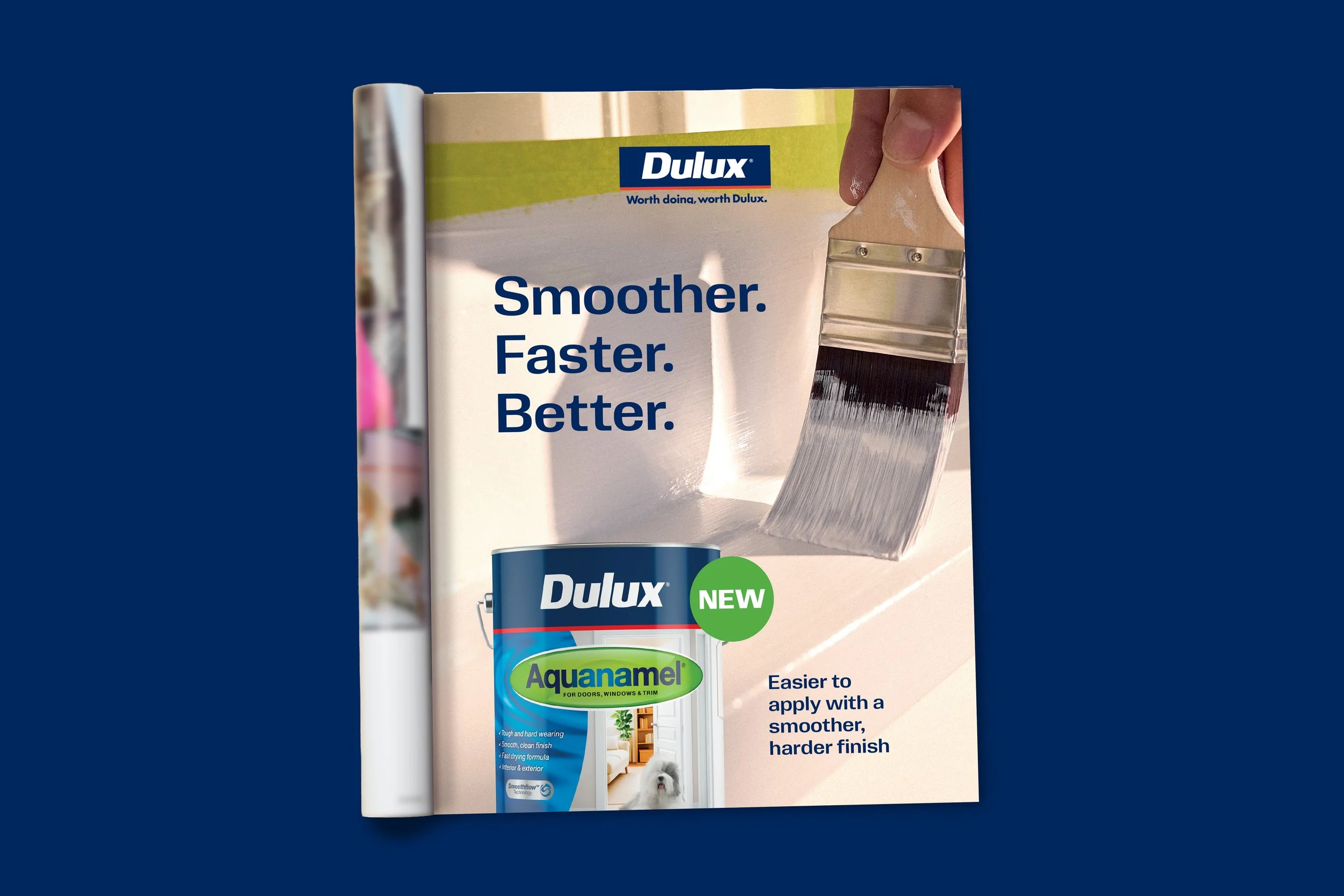 A store display featuring Dulux paint products and a paintbrush applying white paint on a wall, with the slogan 'Smoother. Faster. Better.' and a small dog sitting in front.