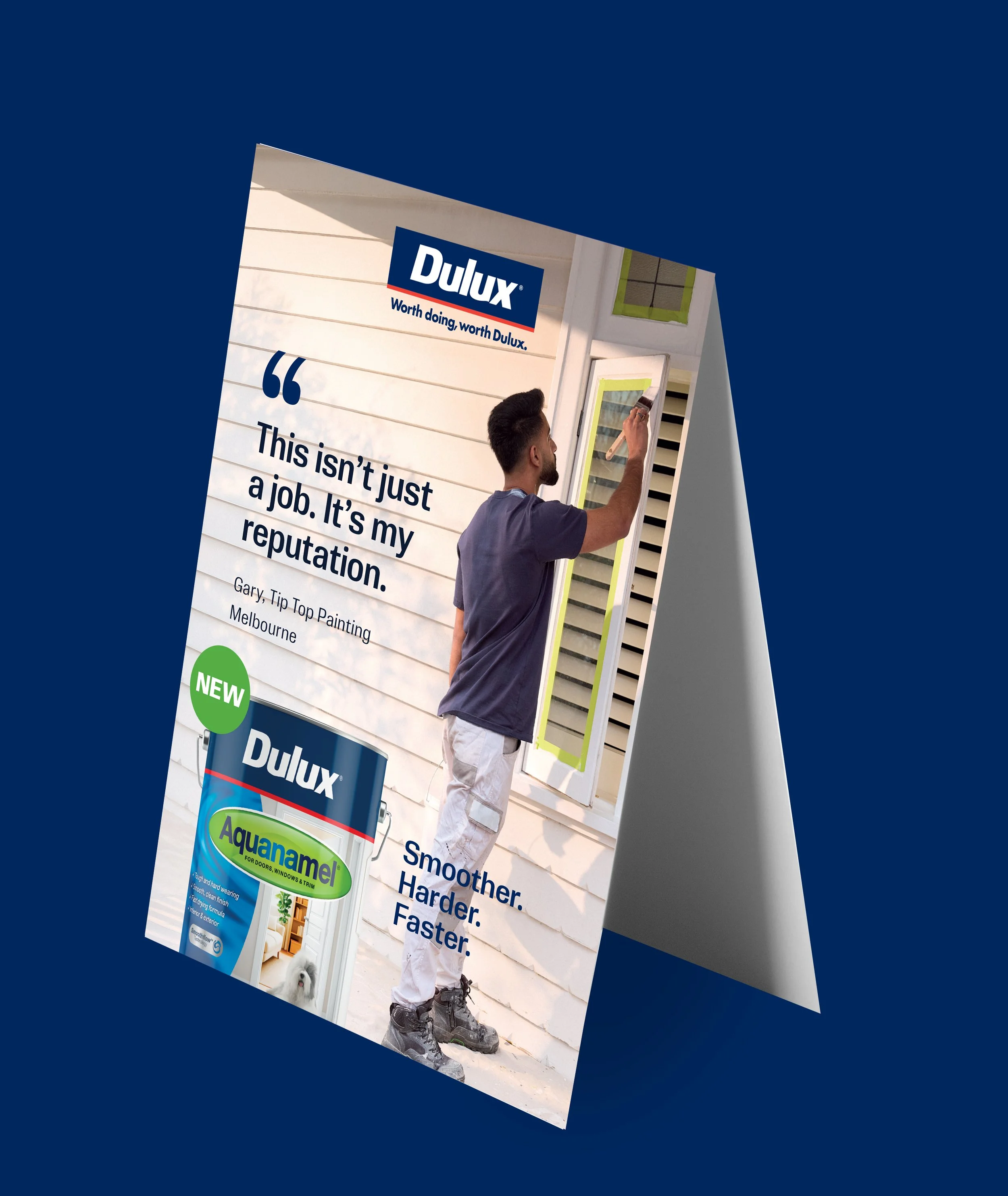 A man installing or painting a window on a house exterior, with a Dulux paint advertisement partially visible in the background.