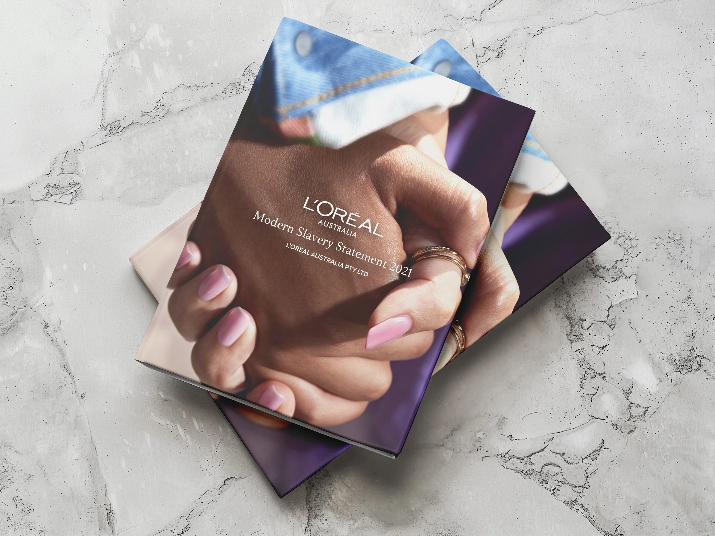 Close-up of a book cover featuring a hand with manicured nails and multiple rings, with the title 'Modern Slavery Statement 2021' and the brand 'L'Oréal Australia'.