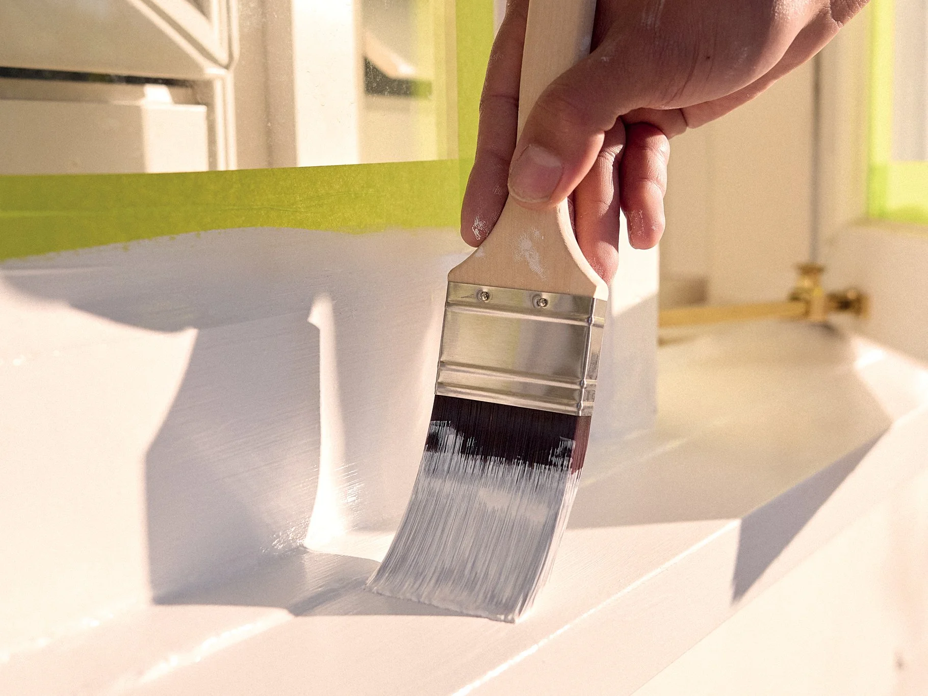 Person applying white paint to a surface with a paintbrush in a well-lit room.