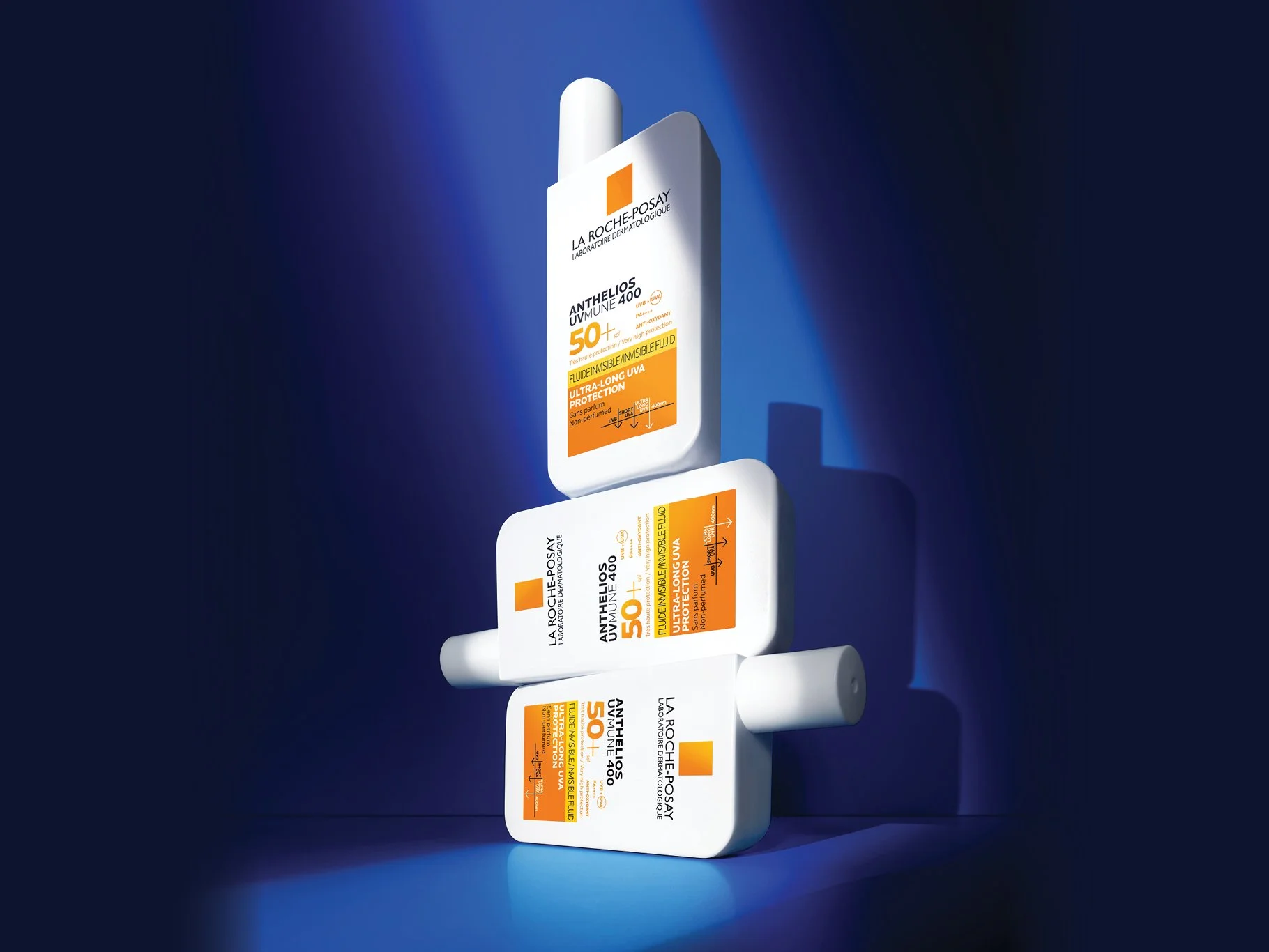 Multiple bottles of La Roche-Posay Anthelios UV Mune 400 SPF 50+ invisible fluid sunscreen arranged in a row against a dark blue background.