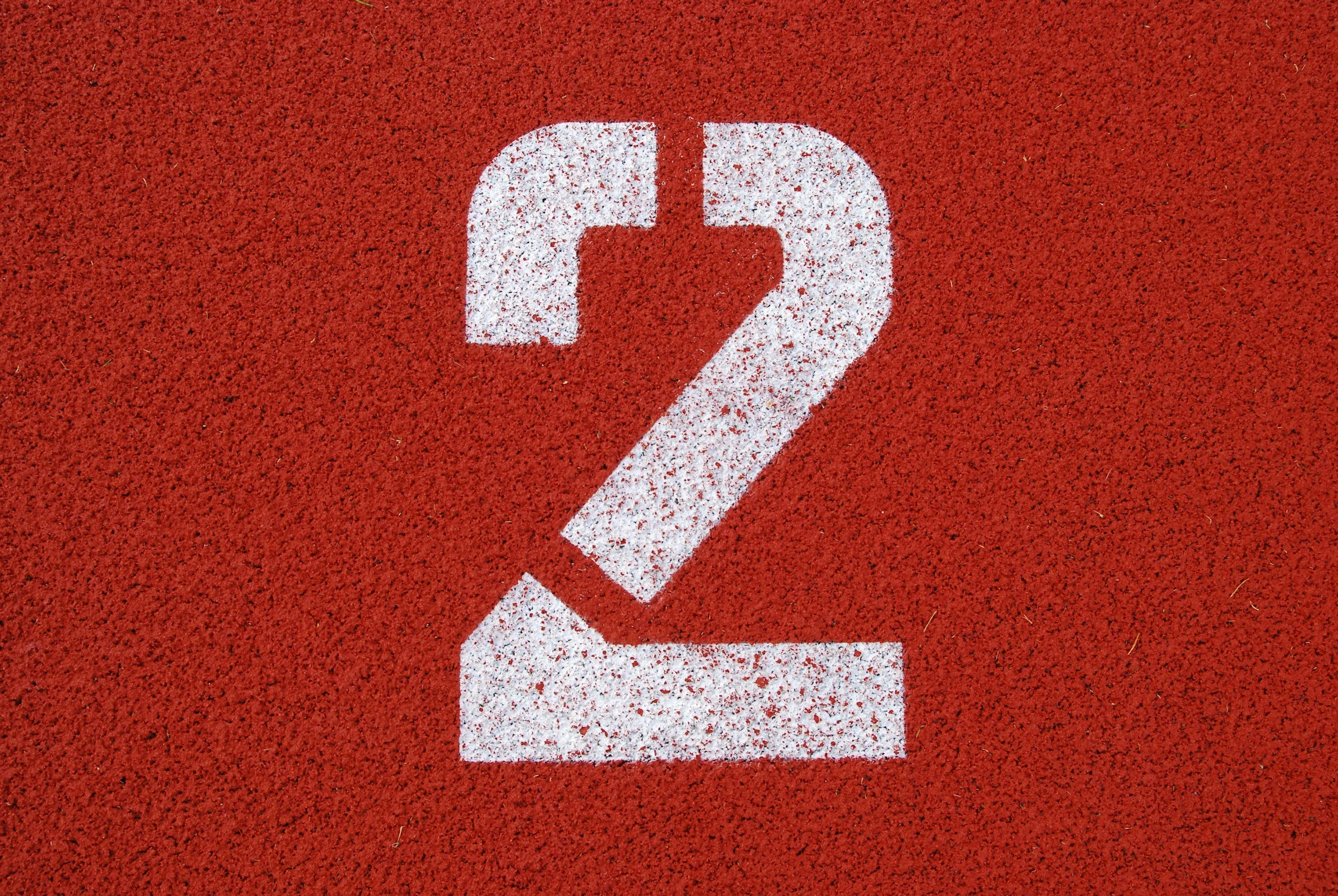 Numéro 2 en blanc sur une surface rouge, probablement une piste de course ou un sol d'athlétisme.