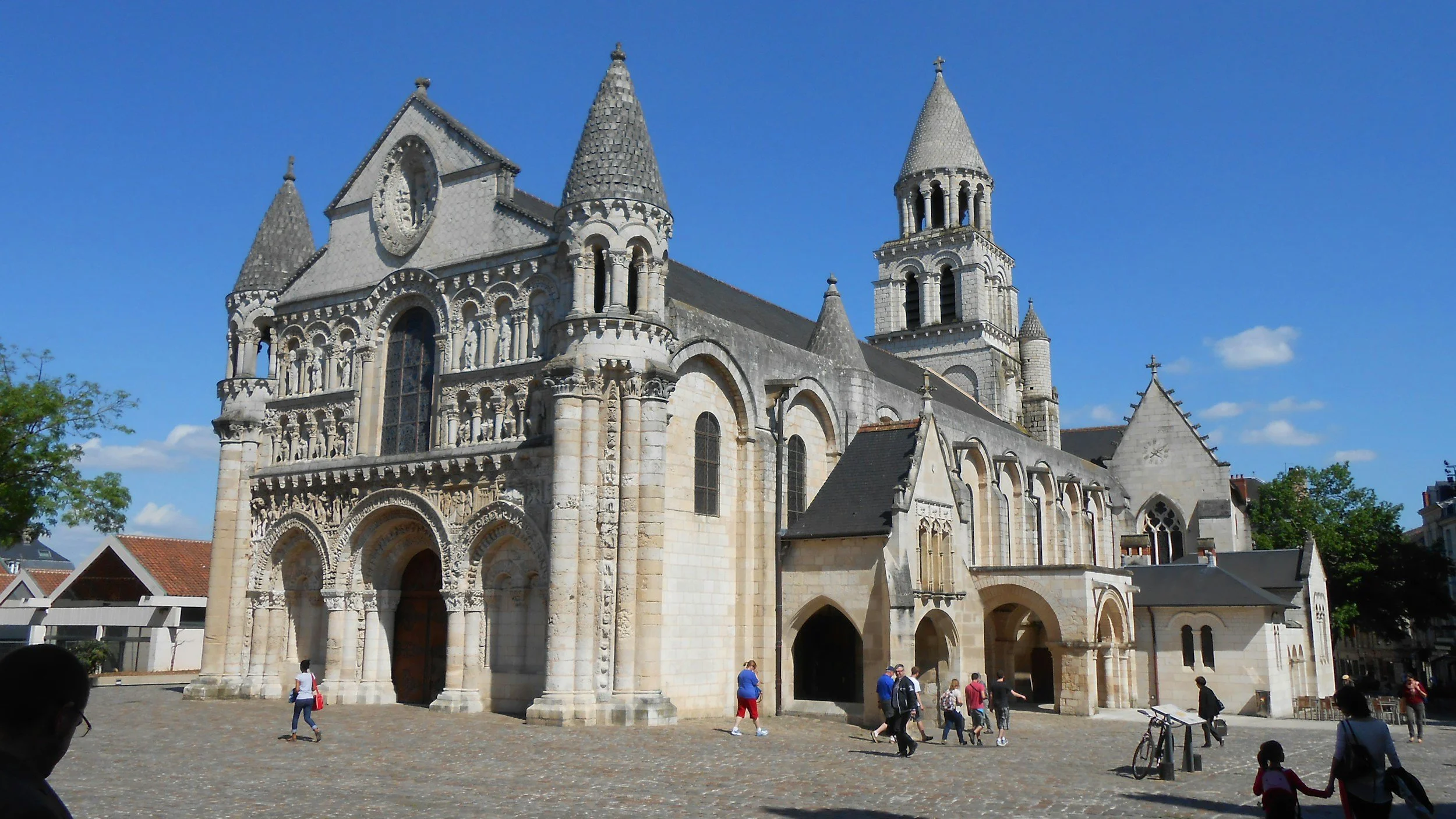 Une ancienne église romane en pierre, avec des tours pointues et des fenêtres gothiques, sous un ciel bleu.
