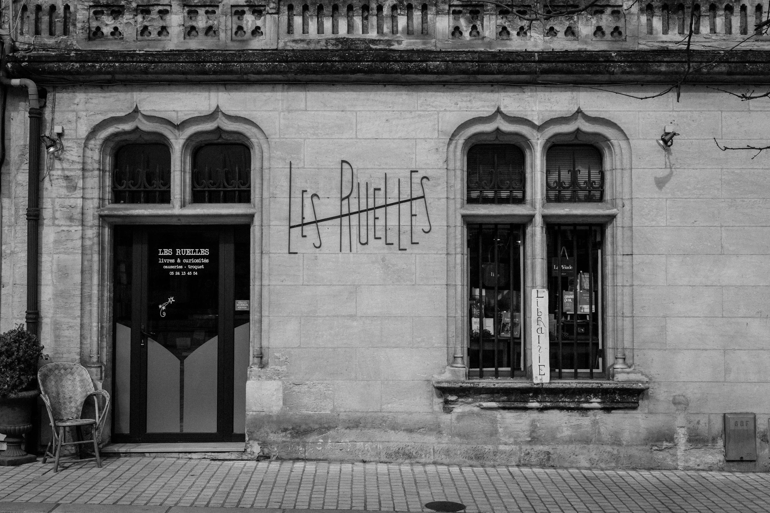 Façade d'une librairie appelée « Les Ruelles » avec deux fenêtres anciennes et un mur en pierre, signalisation en métal indiquant « Librairie ».