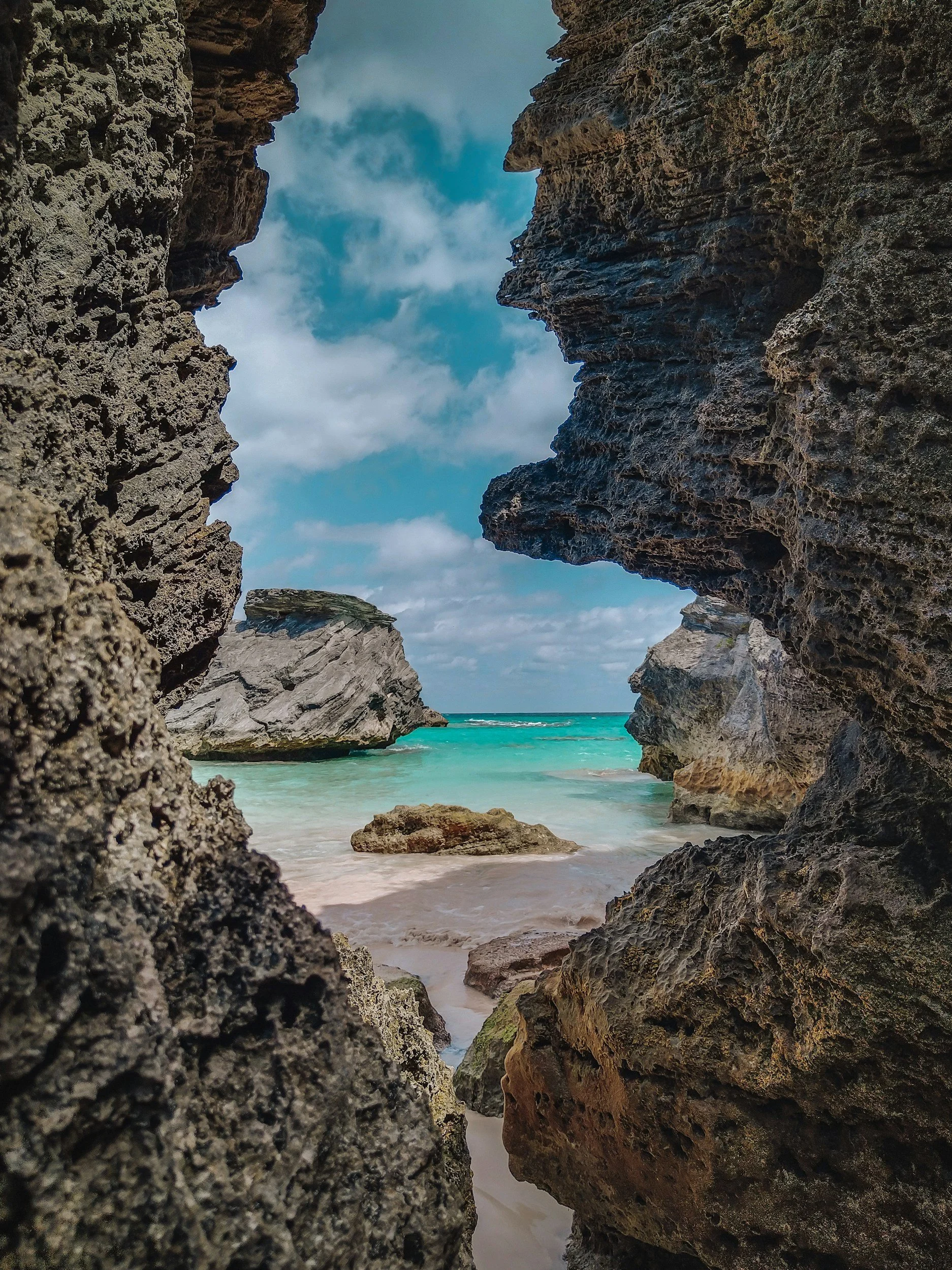 View of a beach with turquoise water and rocky cliffs framing the scene, with sparse clouds in the sky.