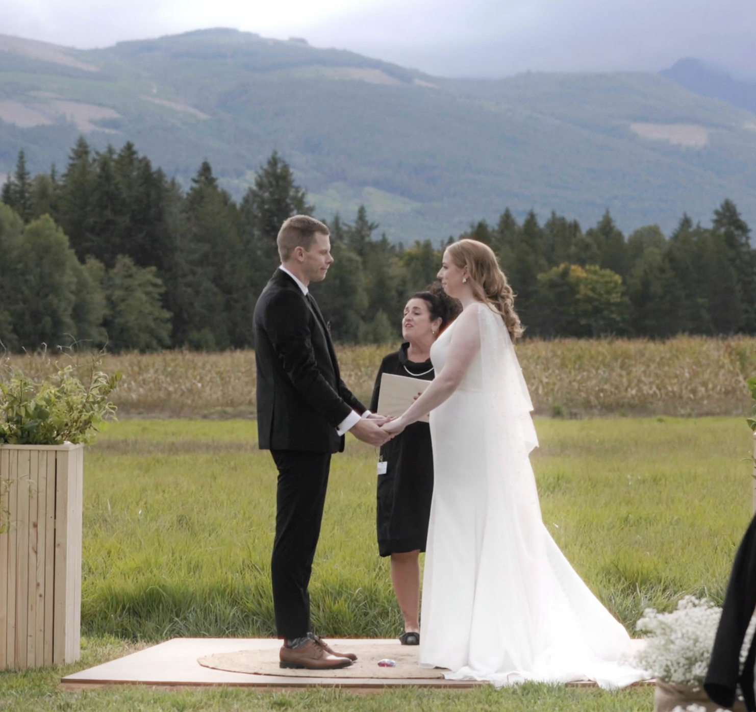 Group of people gathered for a celebration, including a woman in a white wedding dress, surrounded by friends or family, in a wooden venue.