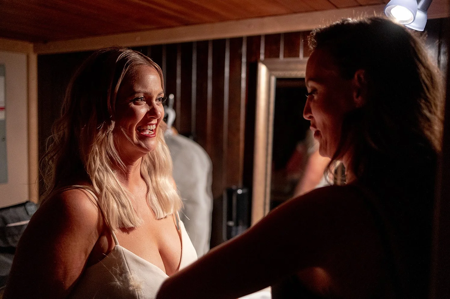 Two women are smiling and engaging in a joyful moment indoors, with warm lighting and a wooden background.