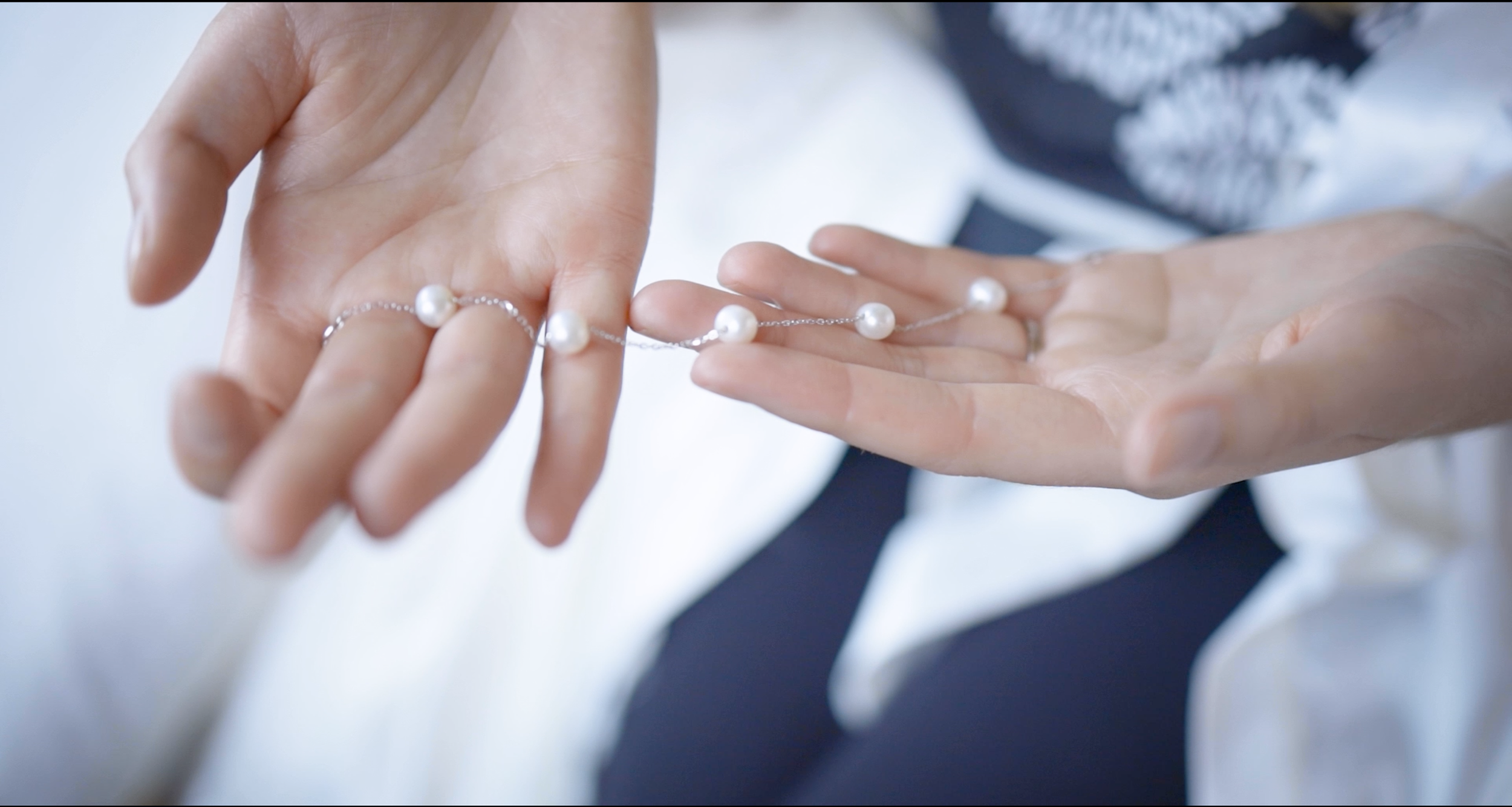 Person holding a pearl necklace with four pearls, one in each hand.