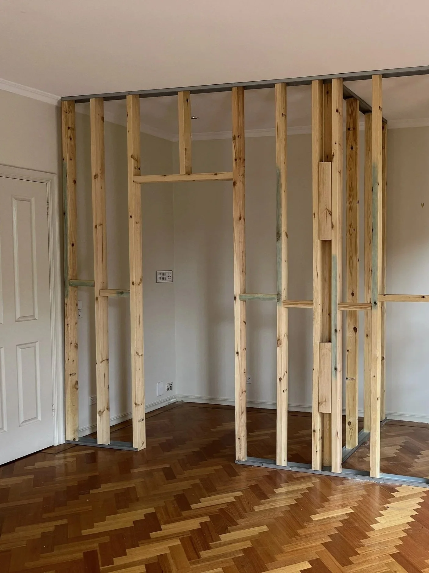 Interior room with exposed wooden framing for a wall or partition, hardwood floor, and a door on the left side.