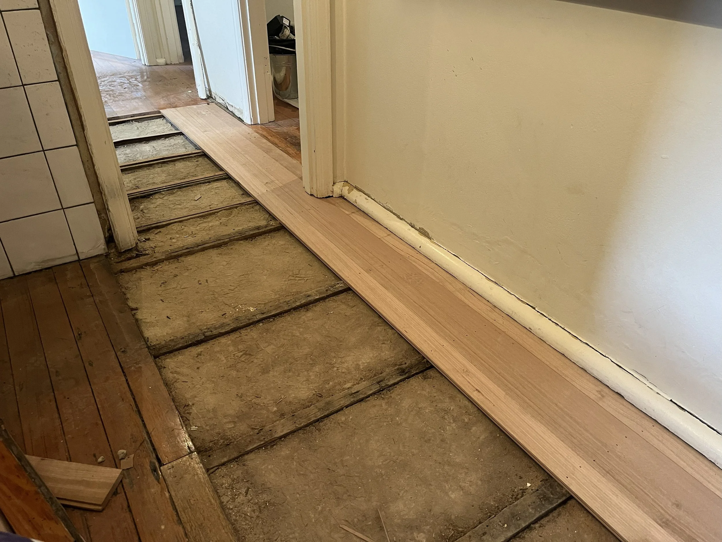 A home renovation where old flooring is being replaced with new wooden flooring at the edge of a doorway.