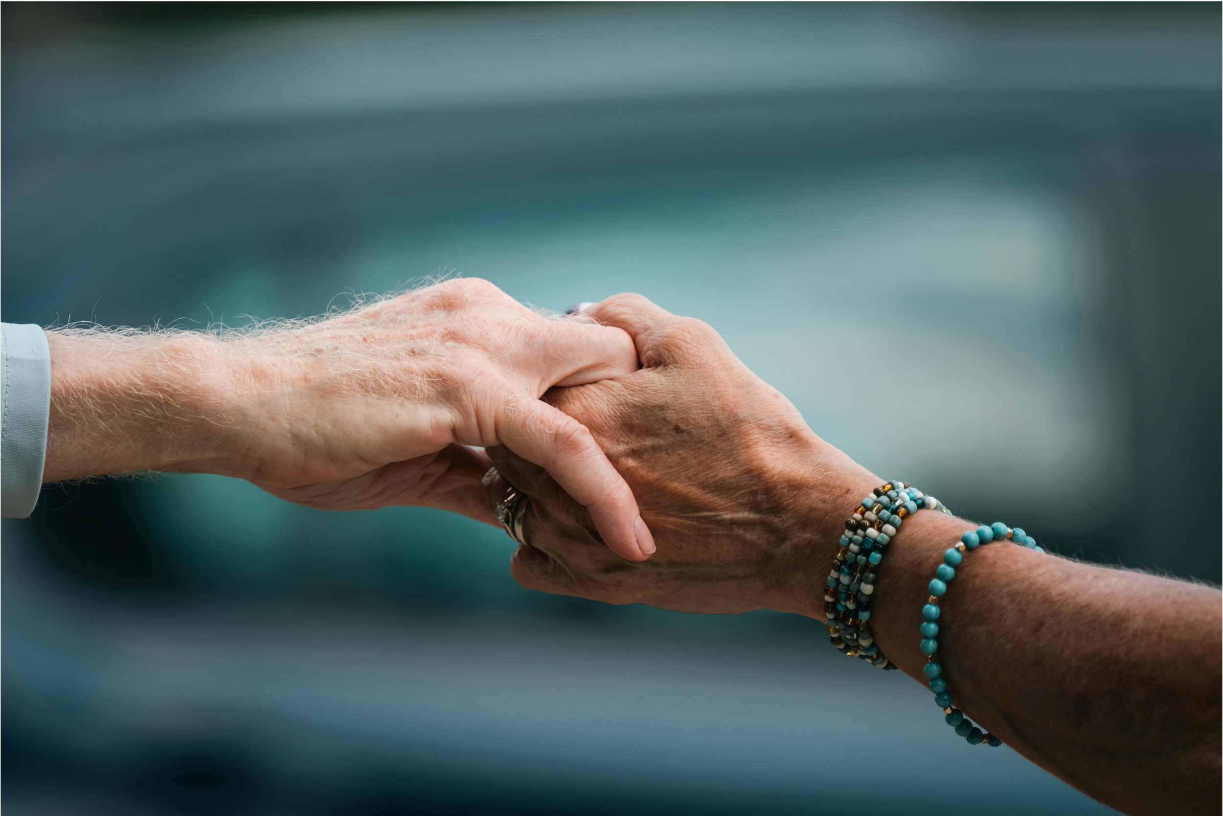 Two hands, one elderly with bracelets, the other younger, clasped together in a handshake.