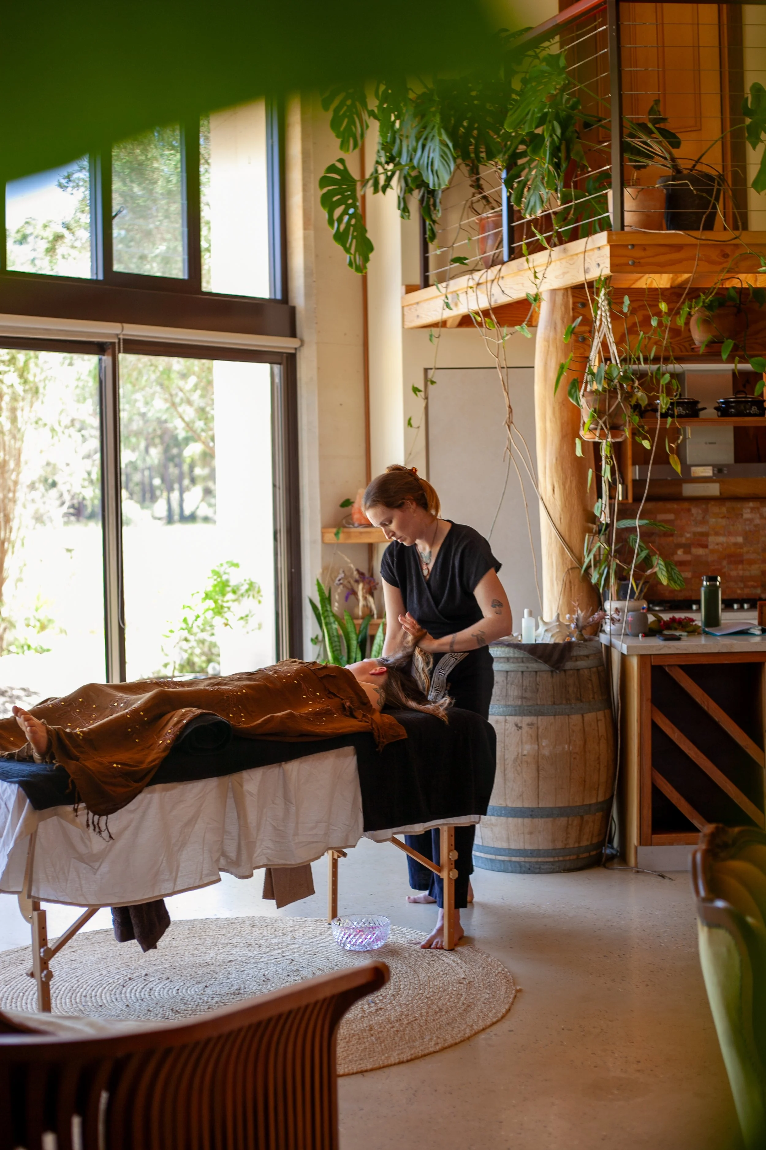 A woman receiving a massage in a cozy, well-lit indoor space decorated with plants and wooden accents.