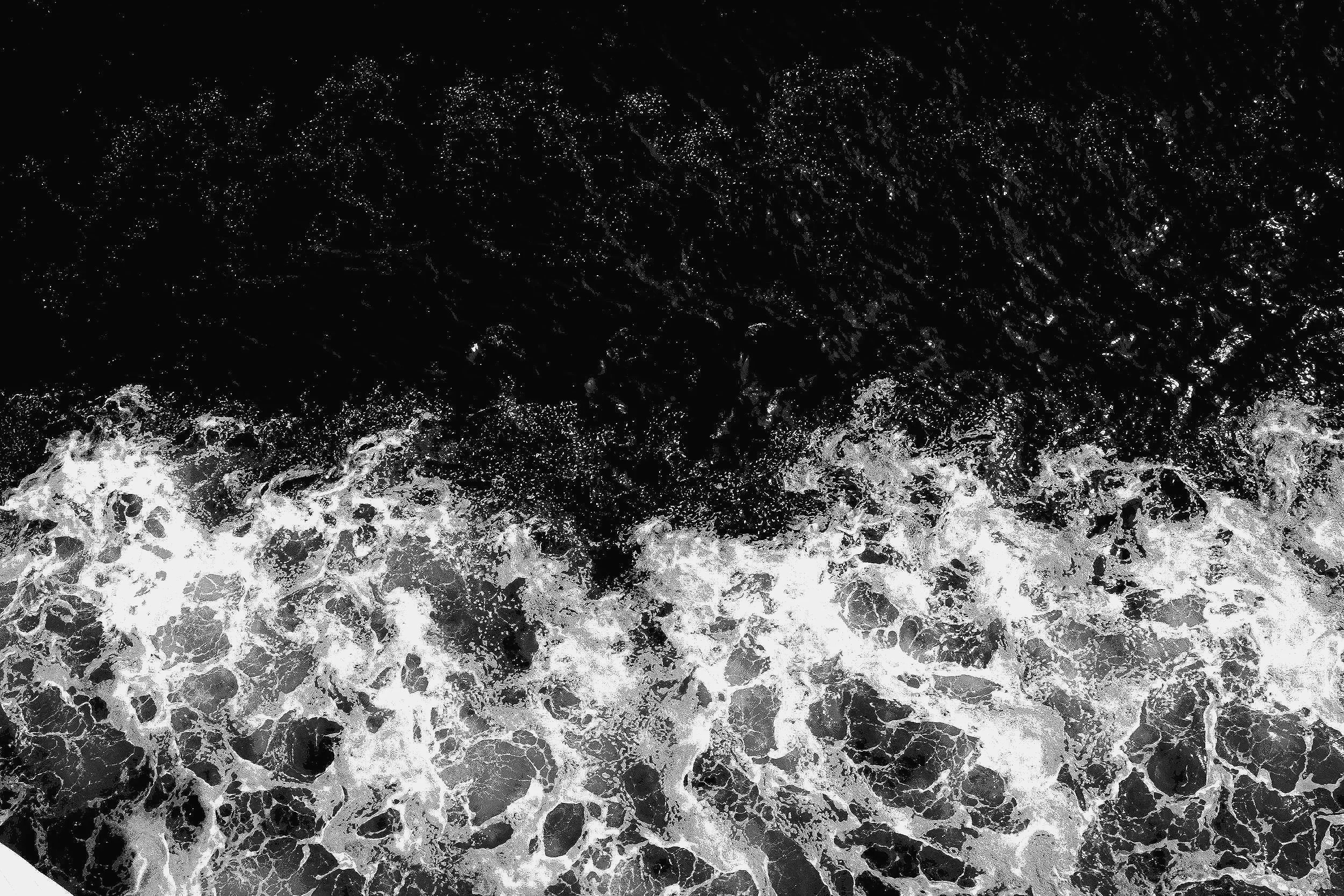 Black and white photograph of ocean waves crashing, with foam and bubbles visible in the water.