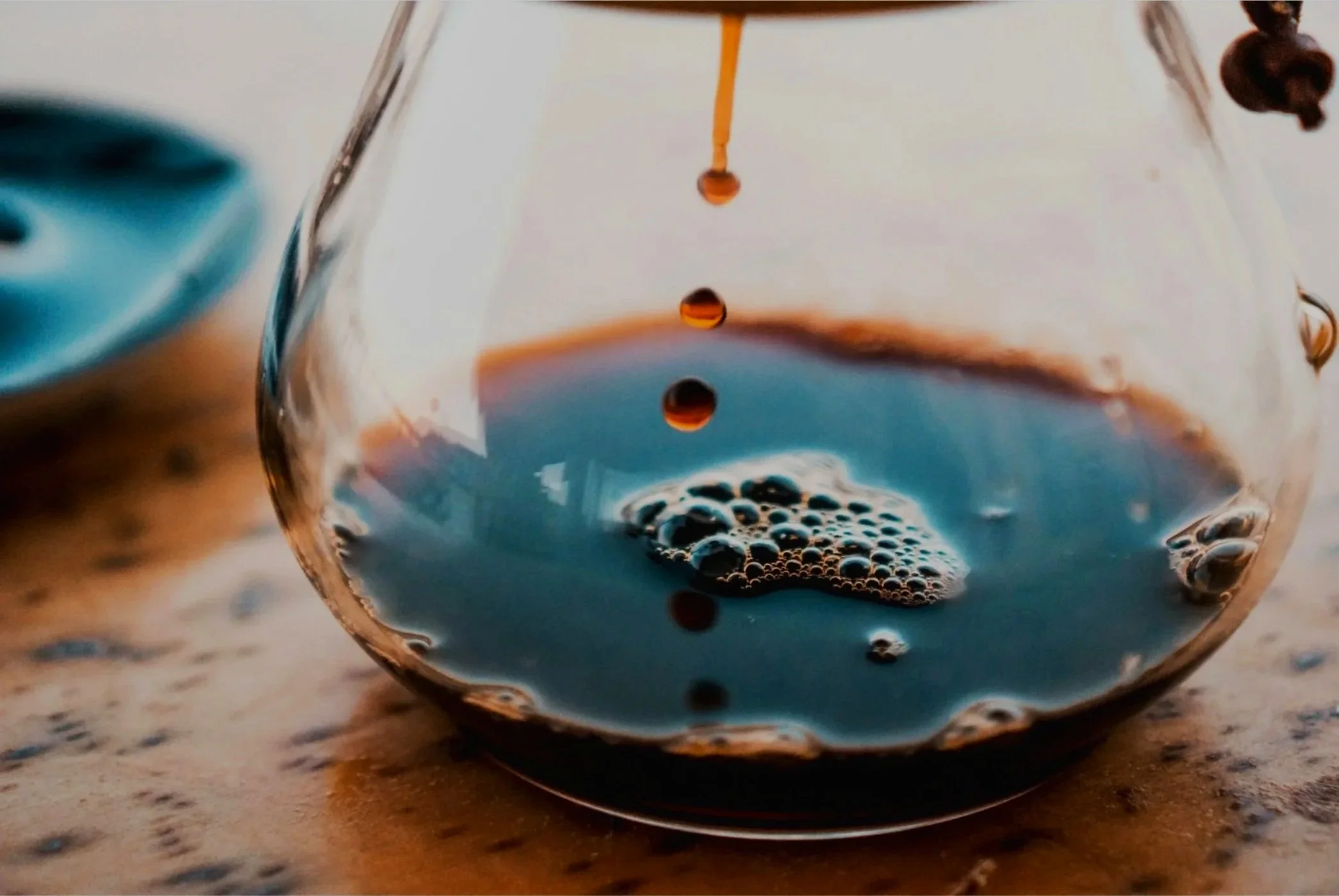 Close-up of black coffee with bubbles inside a clear glass cup, with a scattering of coffee beans on the right side.