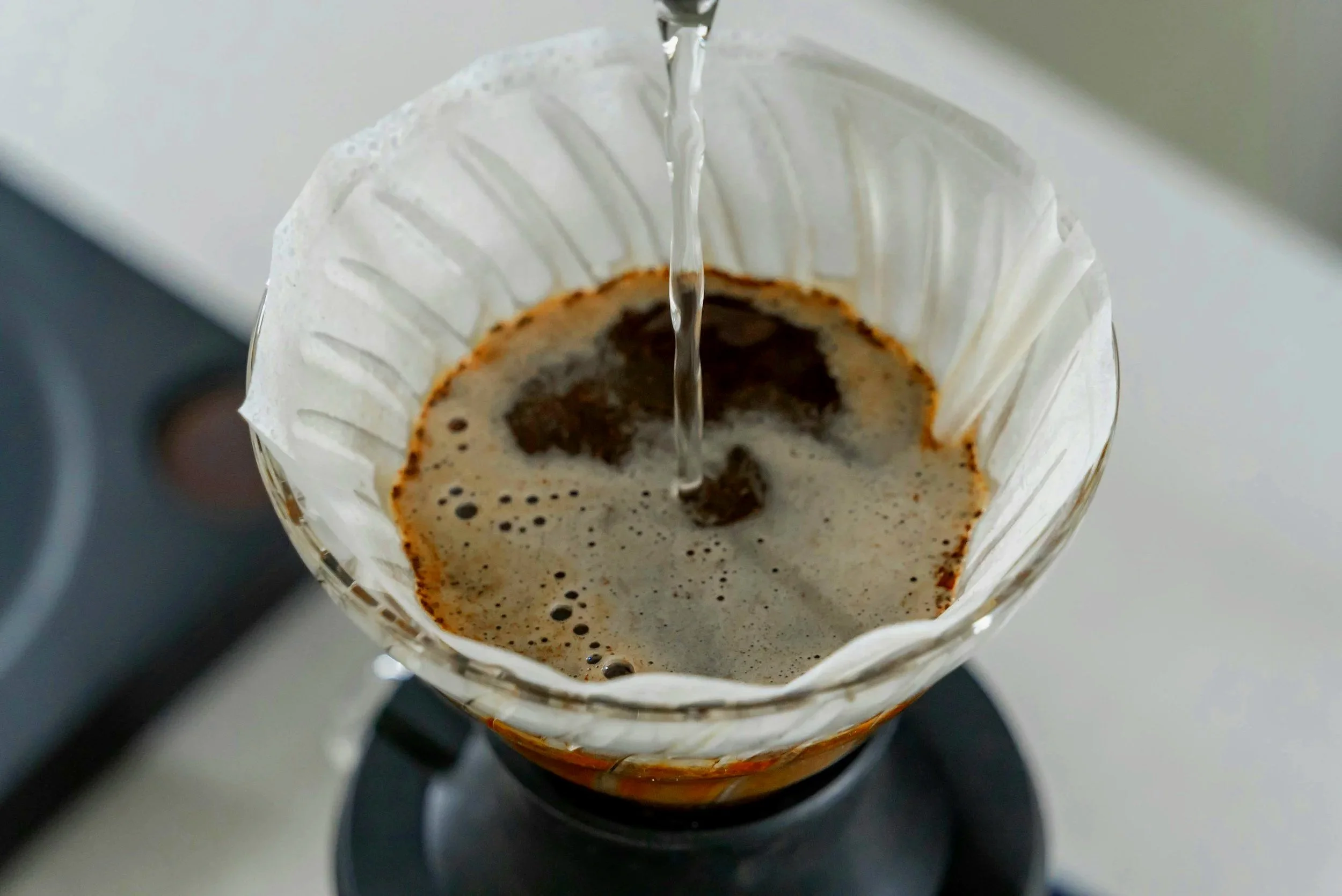 Pouring hot water over coffee grounds in a pour-over coffee maker lined with a paper filter.