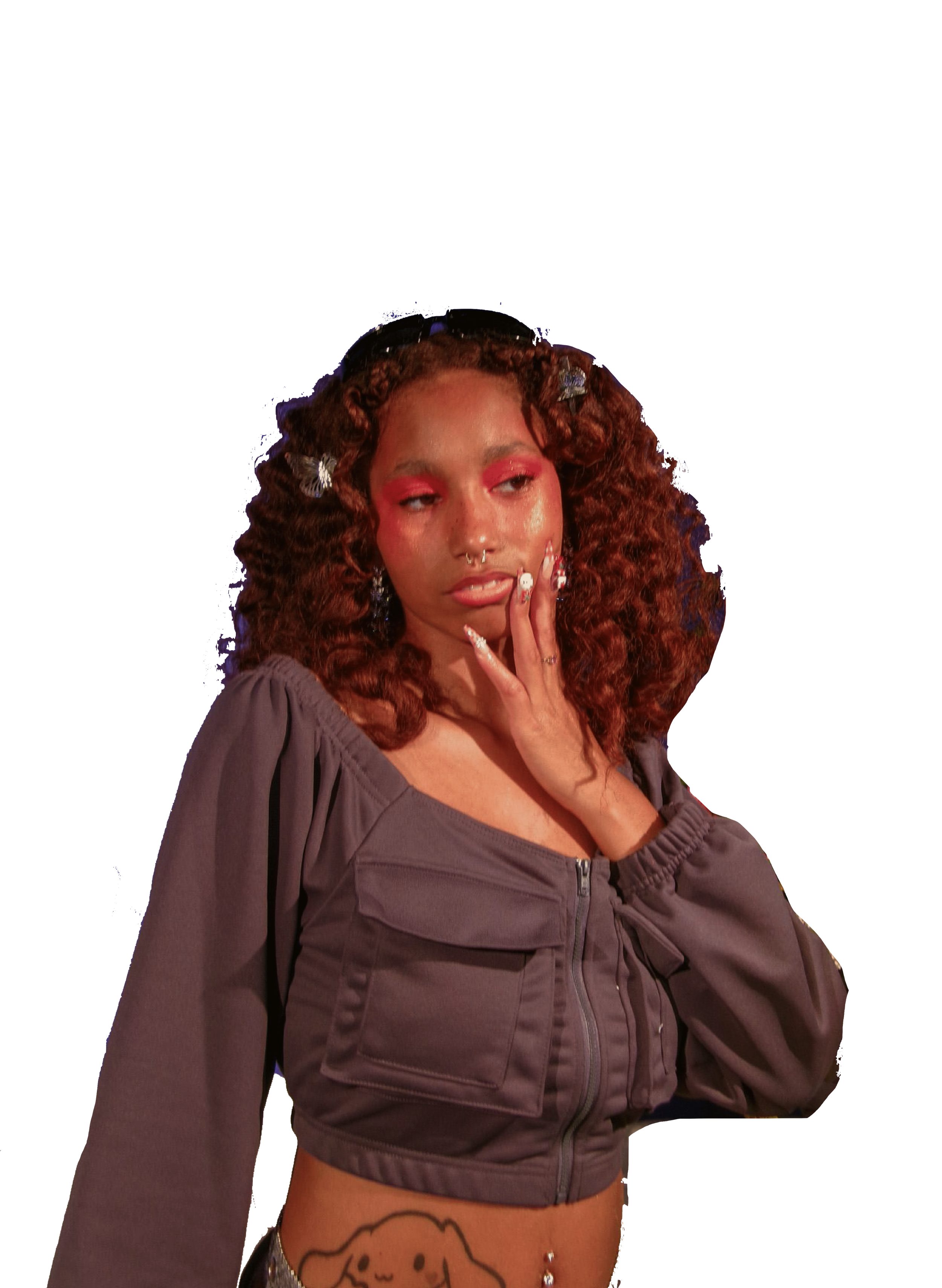 A young woman with curly red hair and makeup, wearing a cropped gray jacket, posing with her hand near her face against a black background.