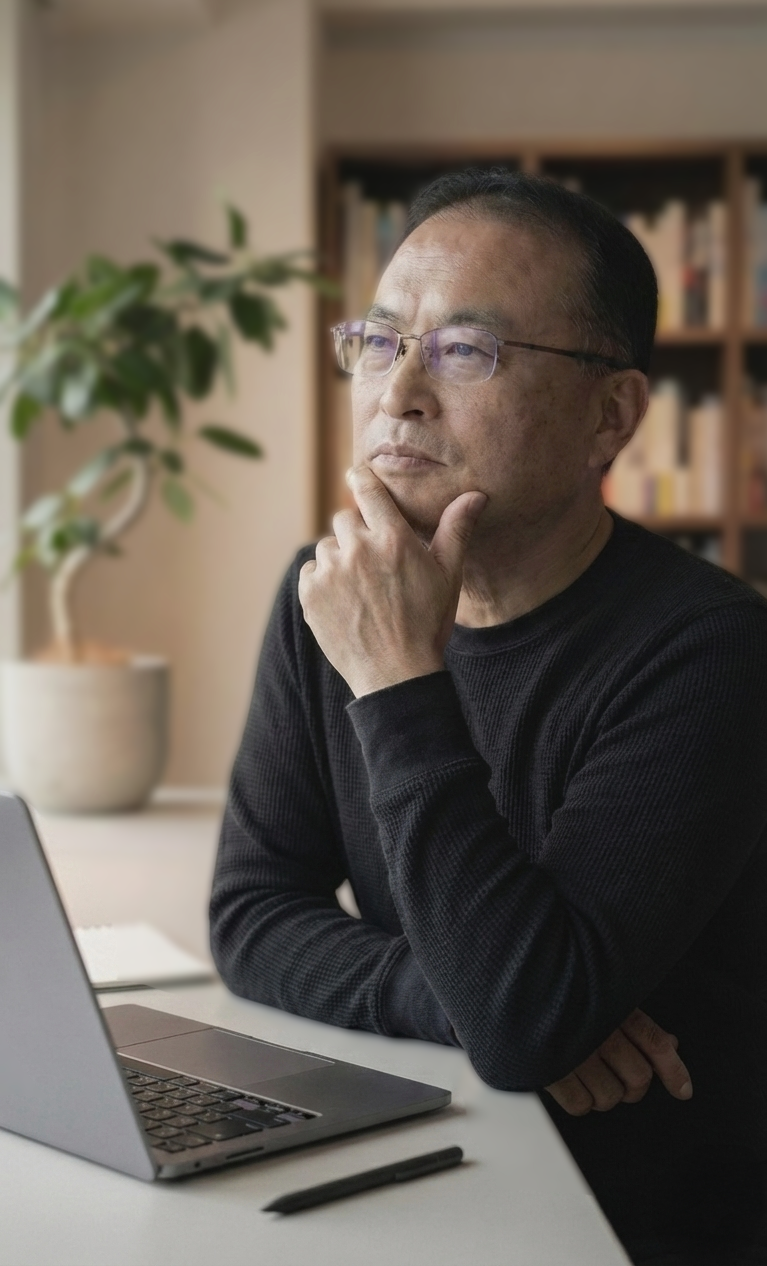 黒いセーターを着た中年の男性が、机に置かれたラップトップを見ながら考え込んでいる。背景には本棚と観葉植物がある。」}}# もちろんです。**画像の内容は、黒いセーターを着た中年の男性が、机に置かれたラップトップを見ながら考え込んでいるところです。背景には本棚と観葉植物があります。**